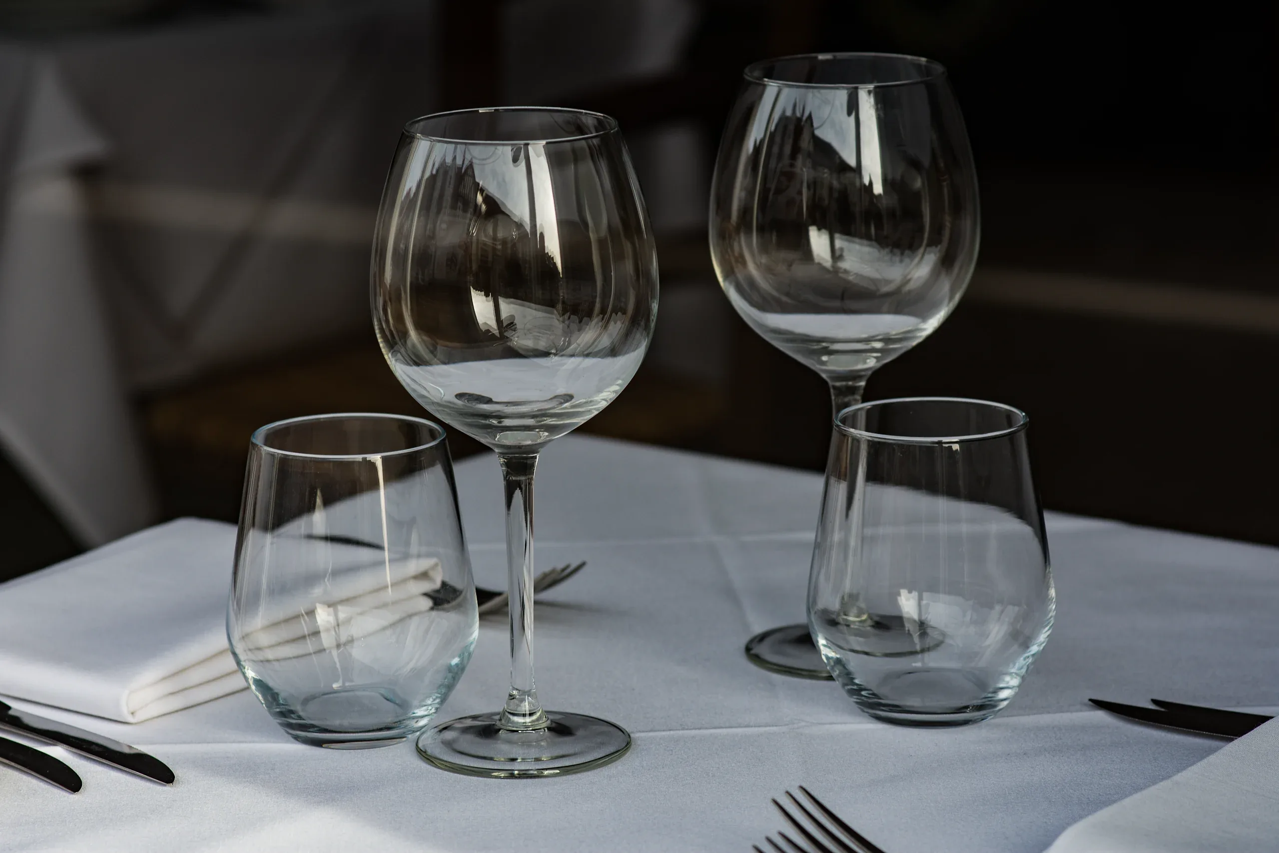 Empty wine and water glasses on a white tablecloth, the room dark behind them