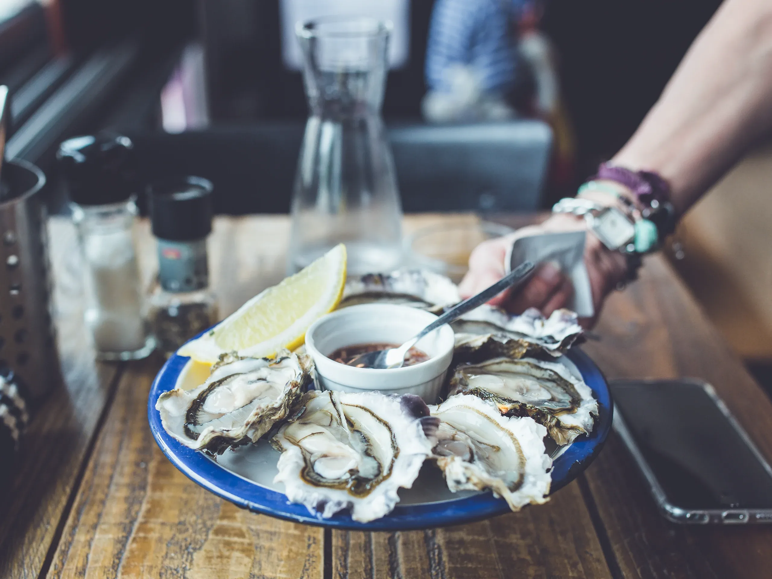 A guest spooning dressing over a plate of oysters and lemon on a wooden bar