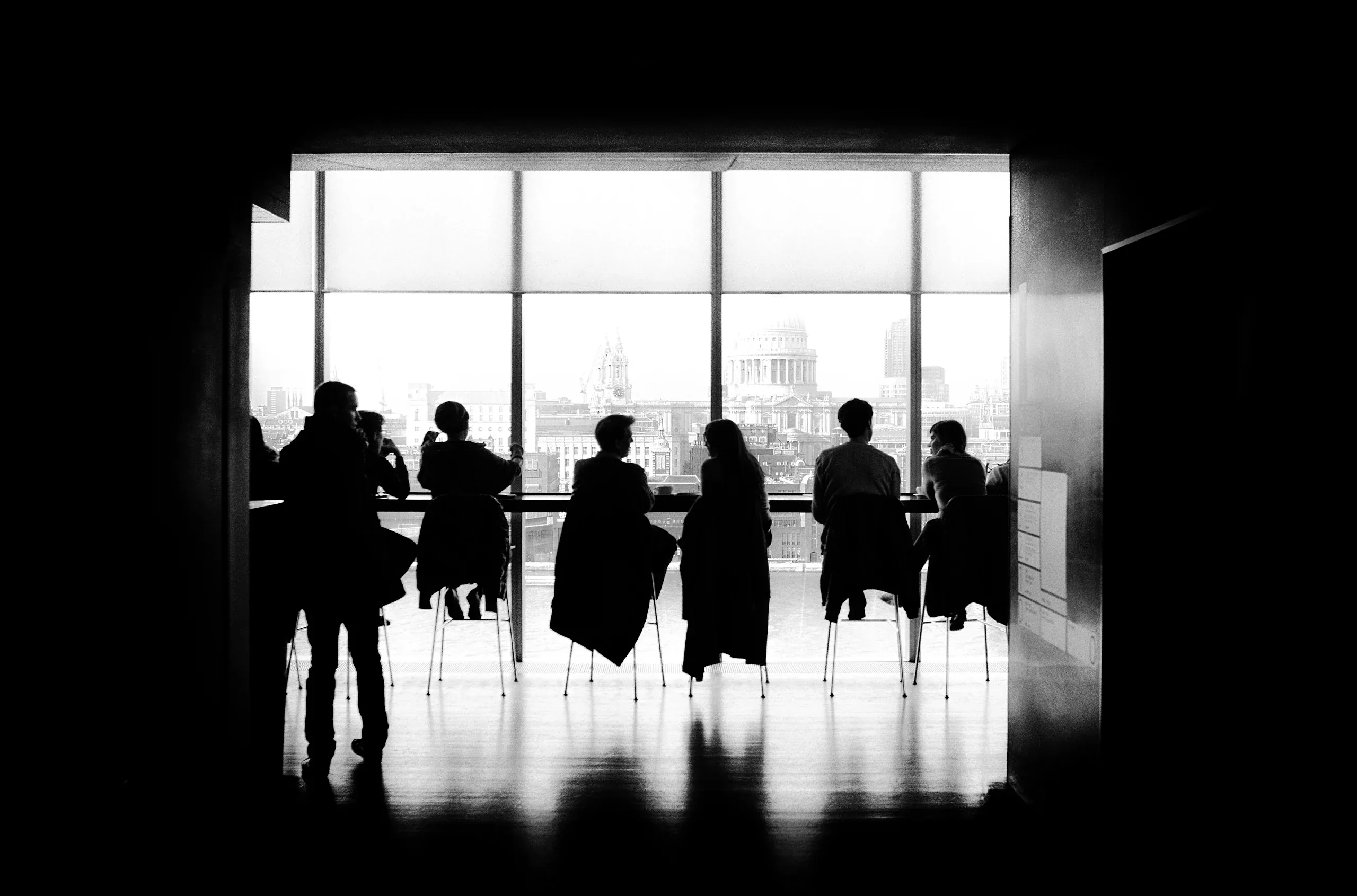 Guests silhouetted at a long table against a tall window over the city