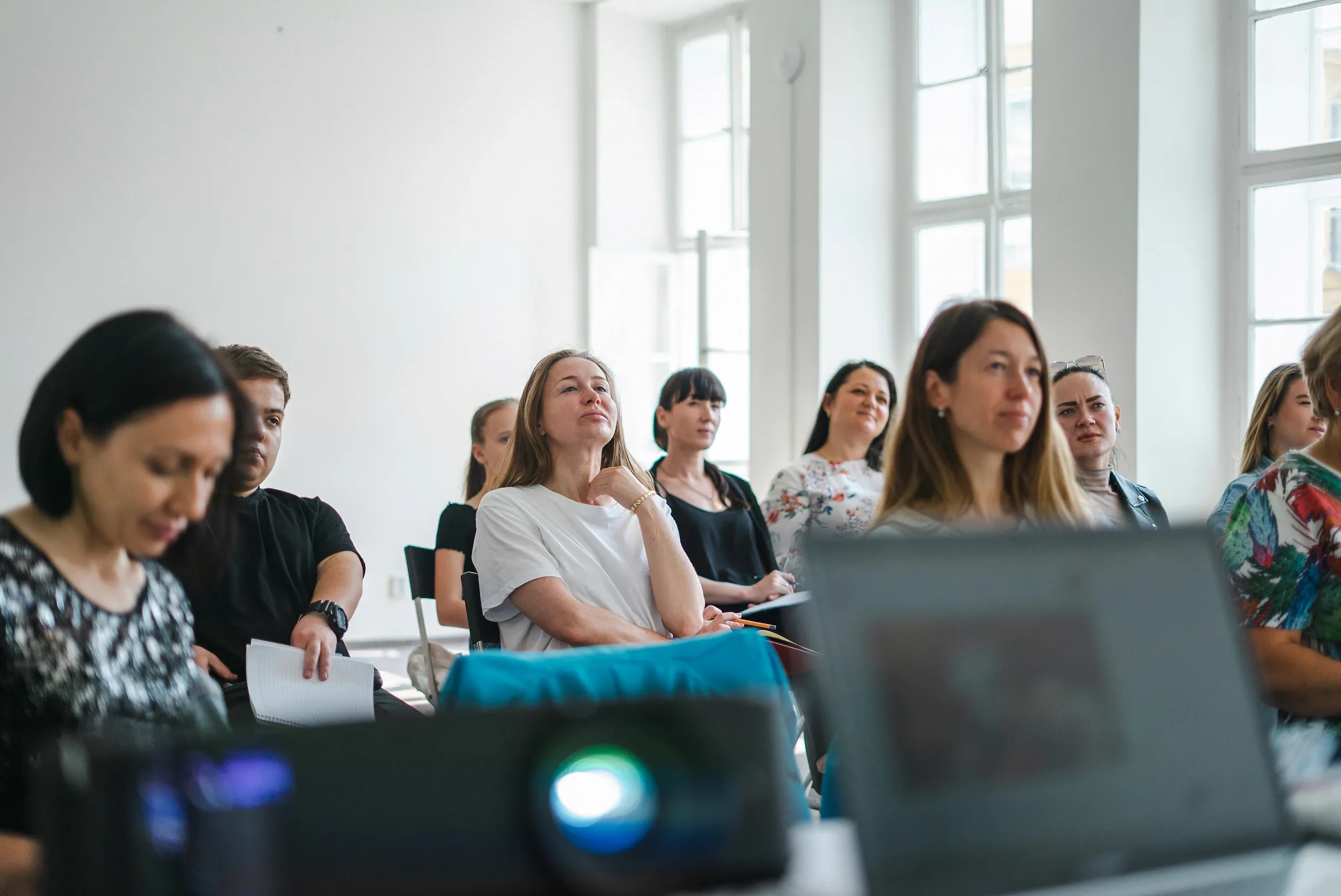 Workshop attendees in a bright room with tall windows, a projector glowing in front of them