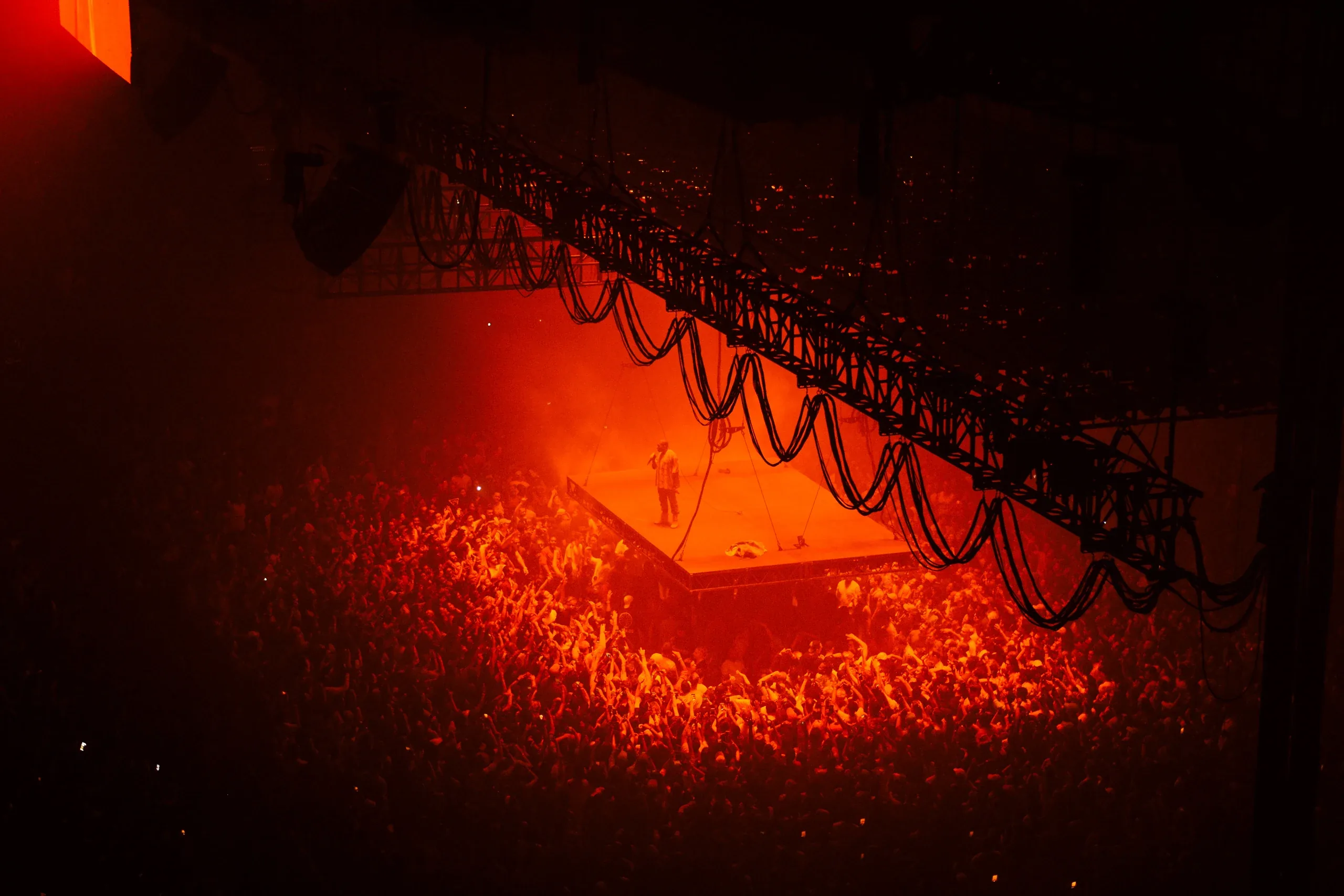 A packed arena floor glowing red under a suspended lighting rig
