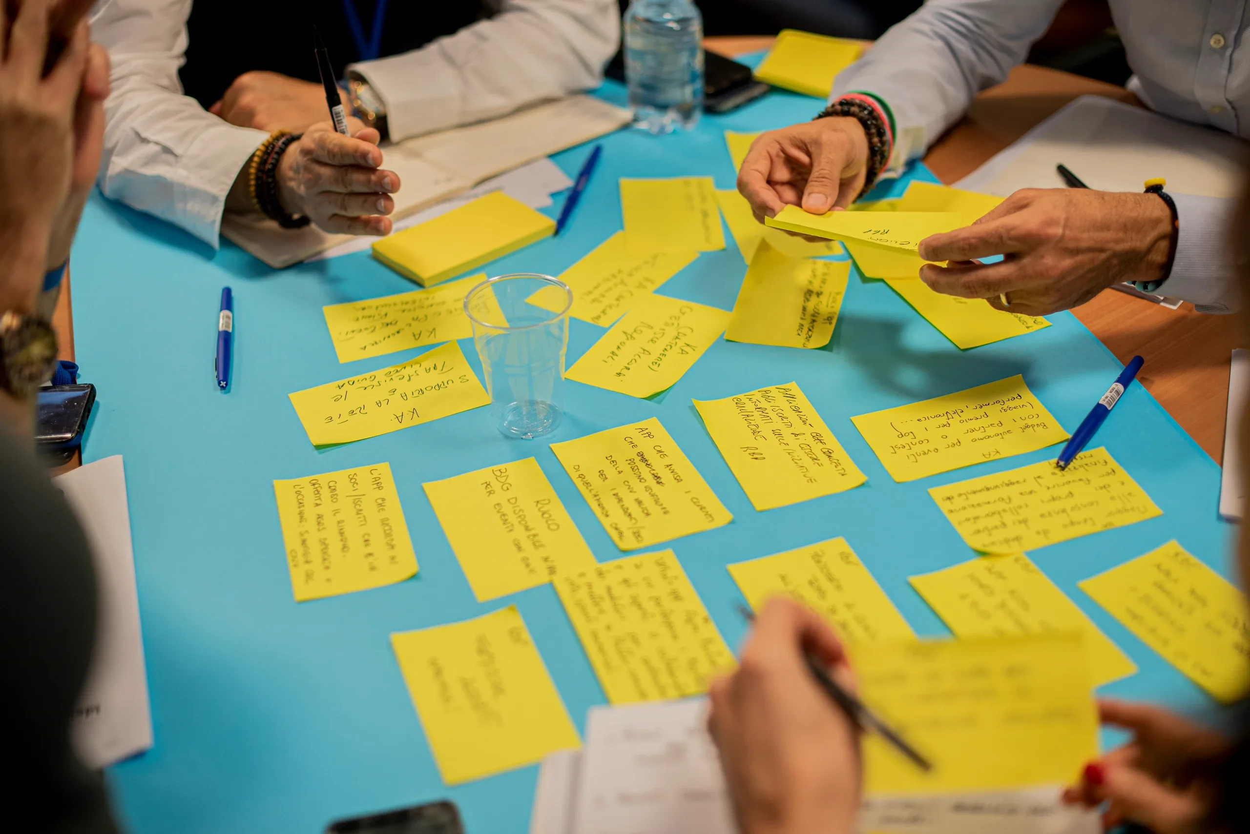 Hands moving yellow sticky notes around a table covered in blue paper during a workshop