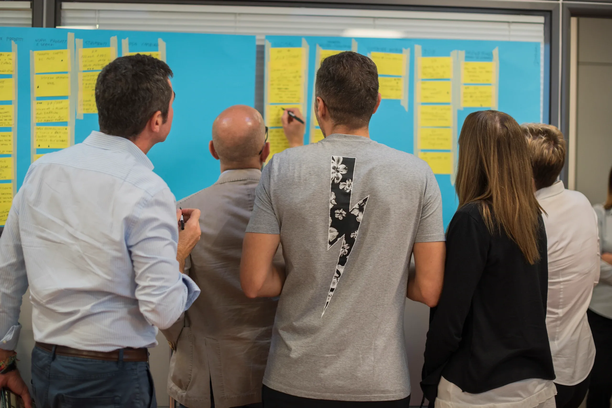 A group standing at a blue wall of yellow sticky notes, one of them writing
