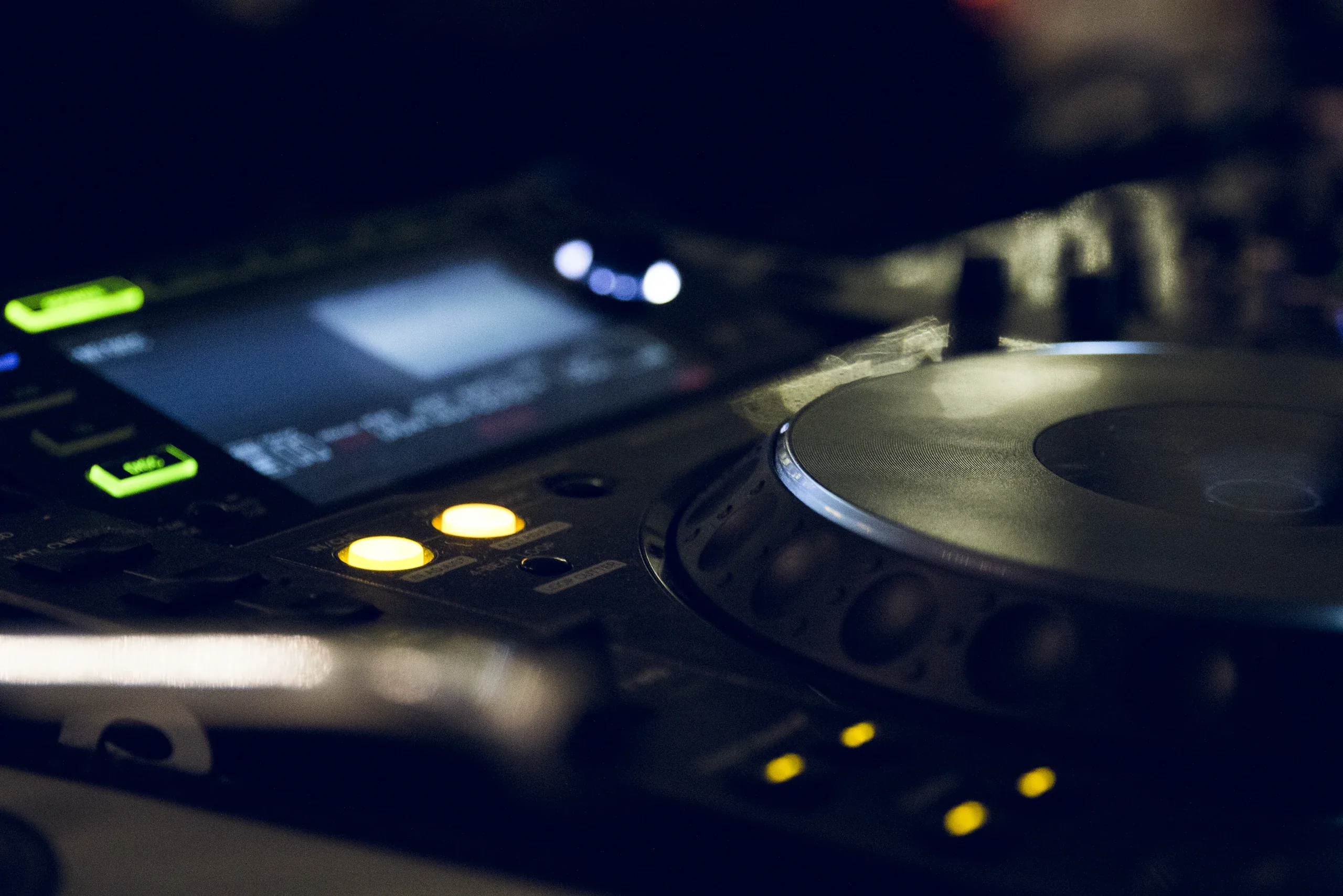 Close-up of a DJ turntable and mixer lit by small green and amber lights