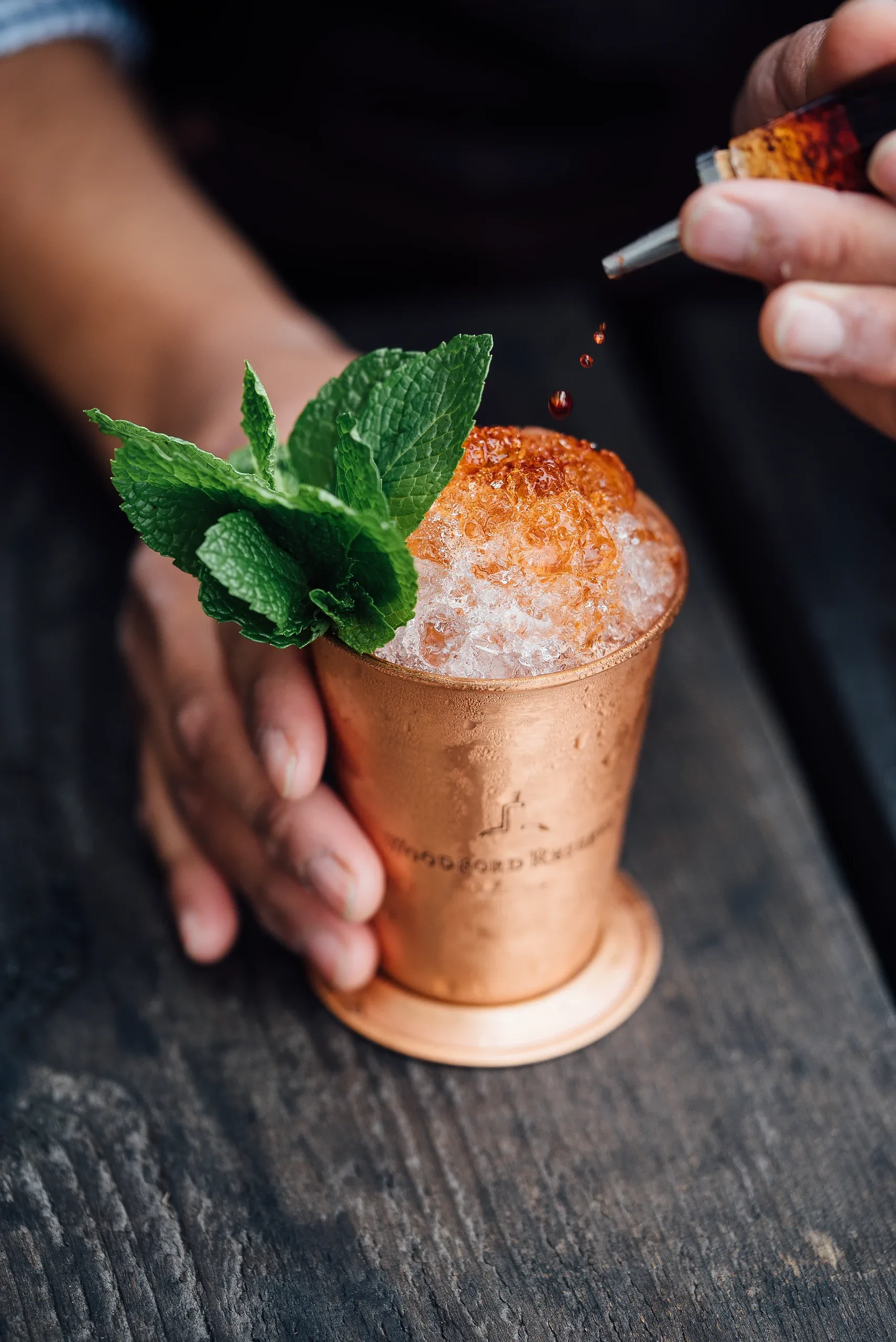 A bartender garnishing a copper cup of crushed ice and mint