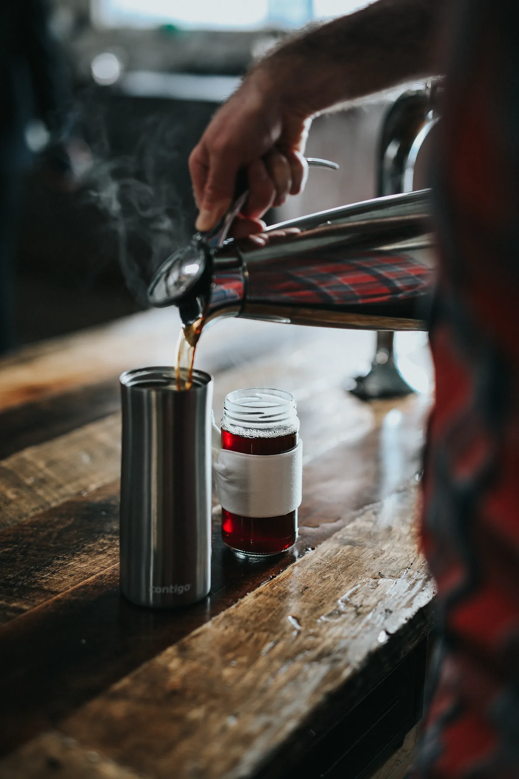 Coffee poured from a steel pot into a tumbler on a wooden bar