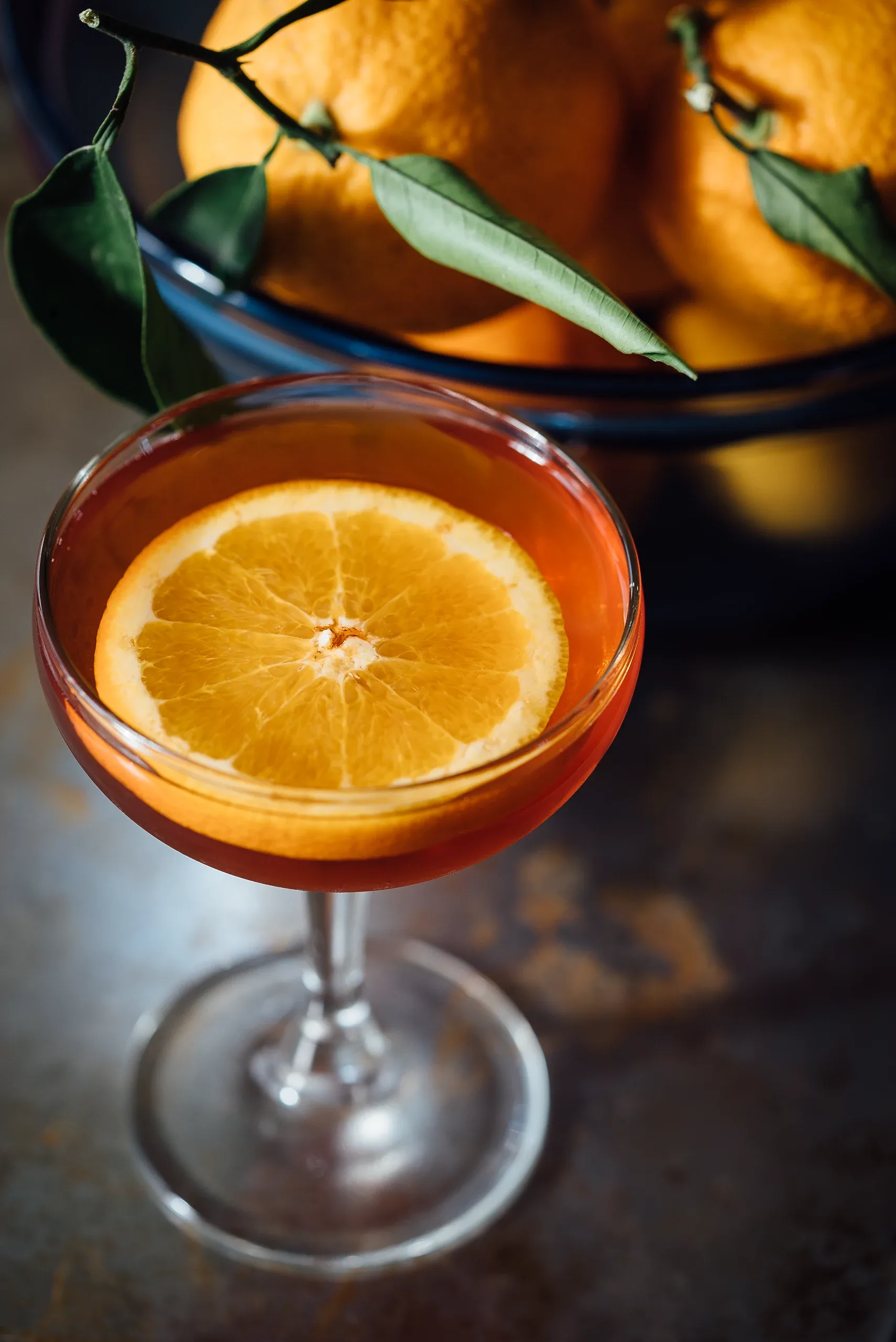An orange slice floating in an amber cocktail in a coupe glass