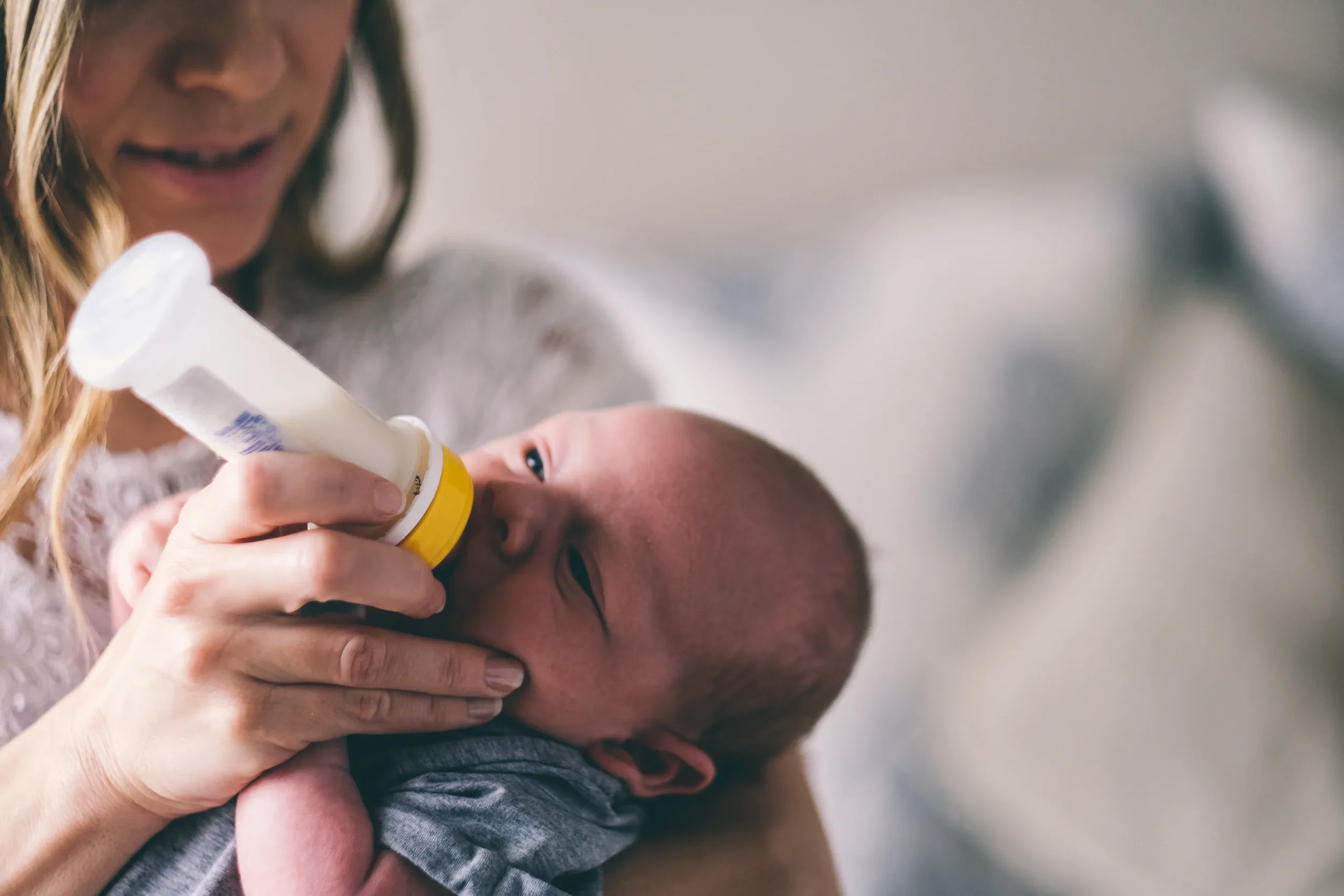Mother bottle feeding her newborn, the baby looking up from her arm