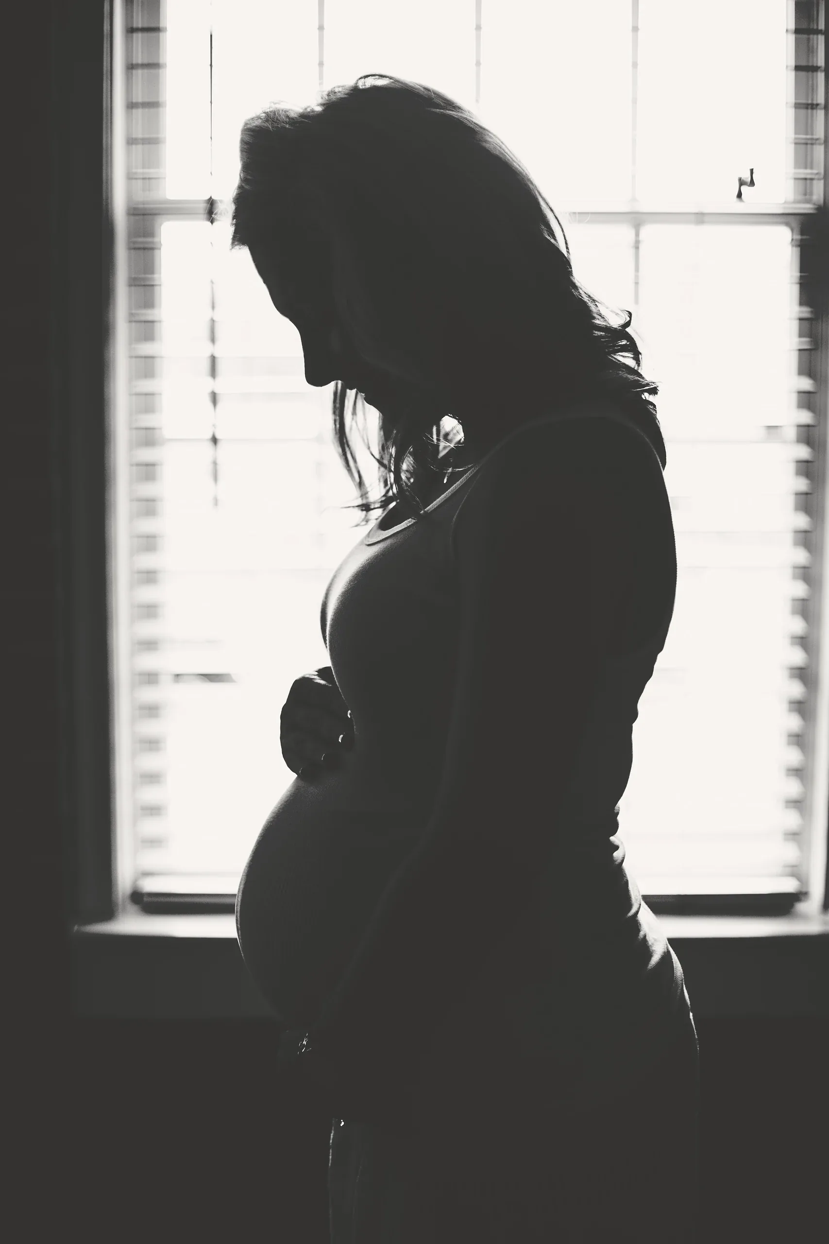 Silhouette of a pregnant woman standing at a bright window
