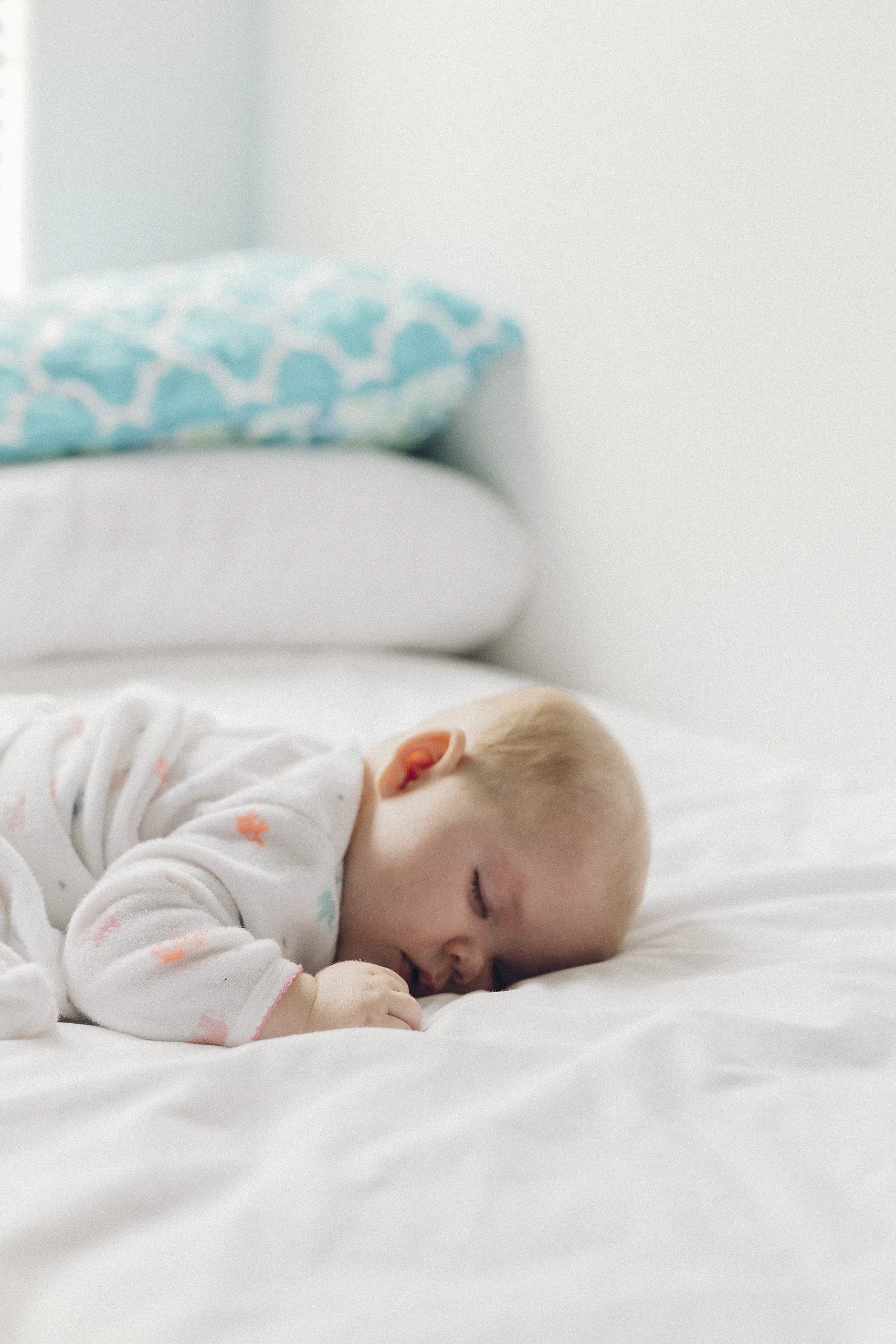 Baby asleep on a white bed beside a soft blue pillow