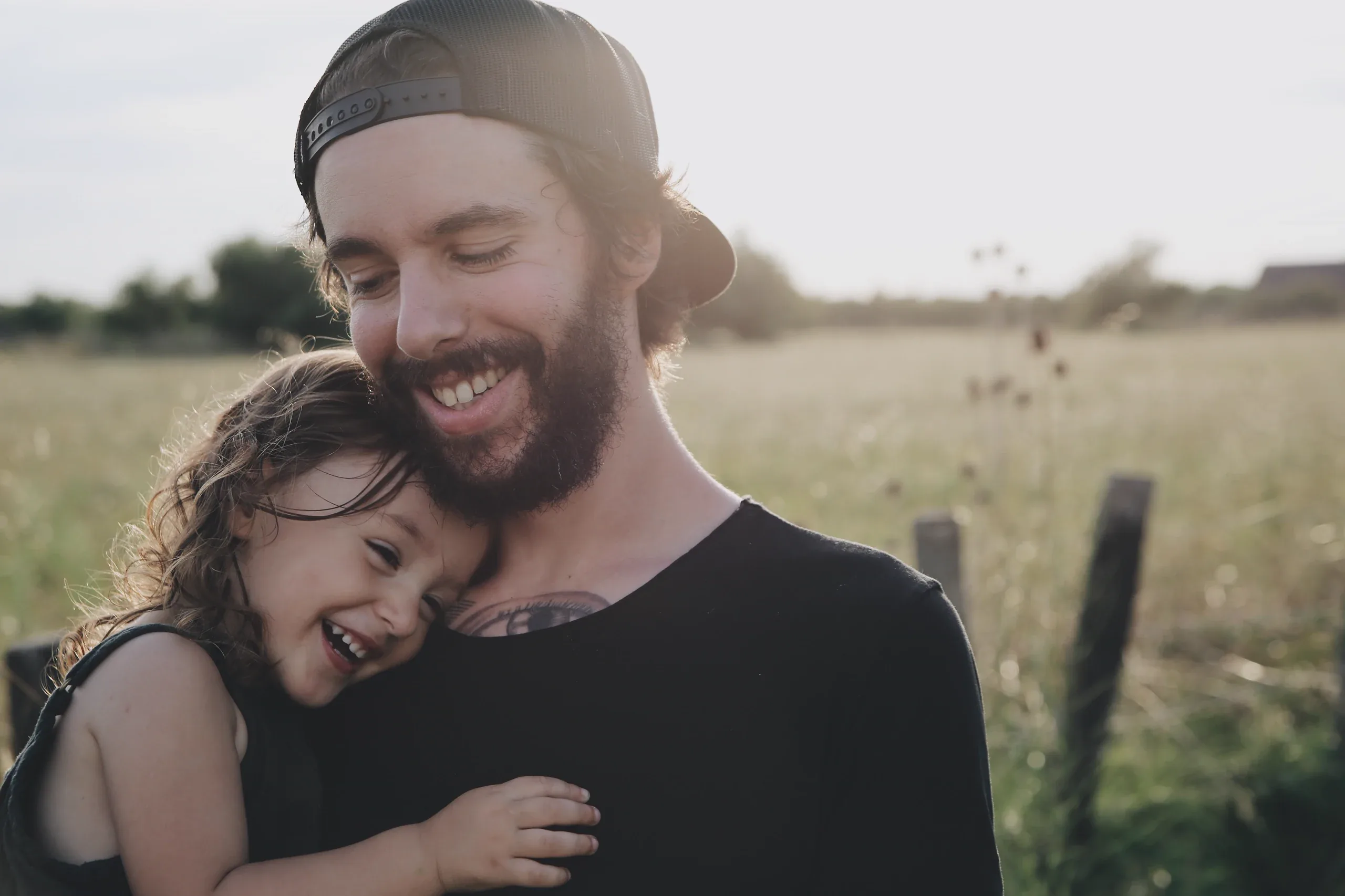 Father hugging his giggling daughter in a summer field