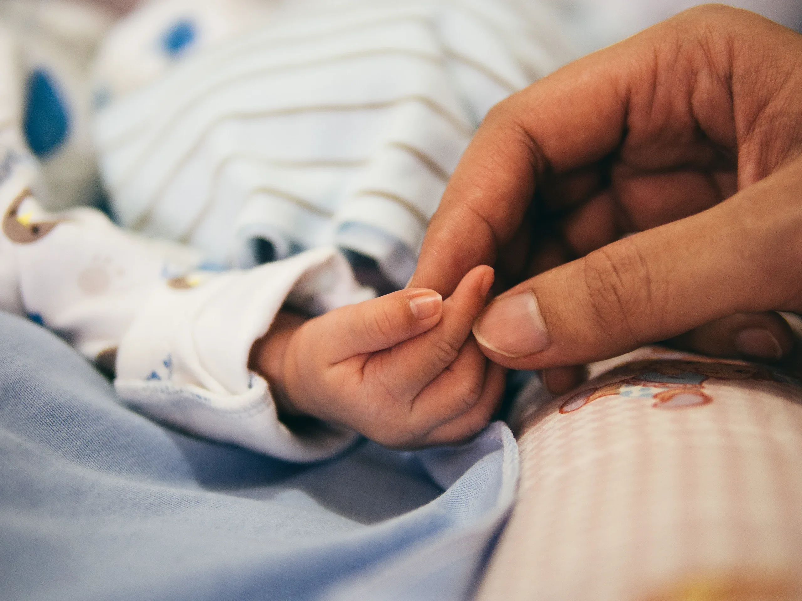 A parent’s fingers holding a newborn’s hand on a striped sleepsuit