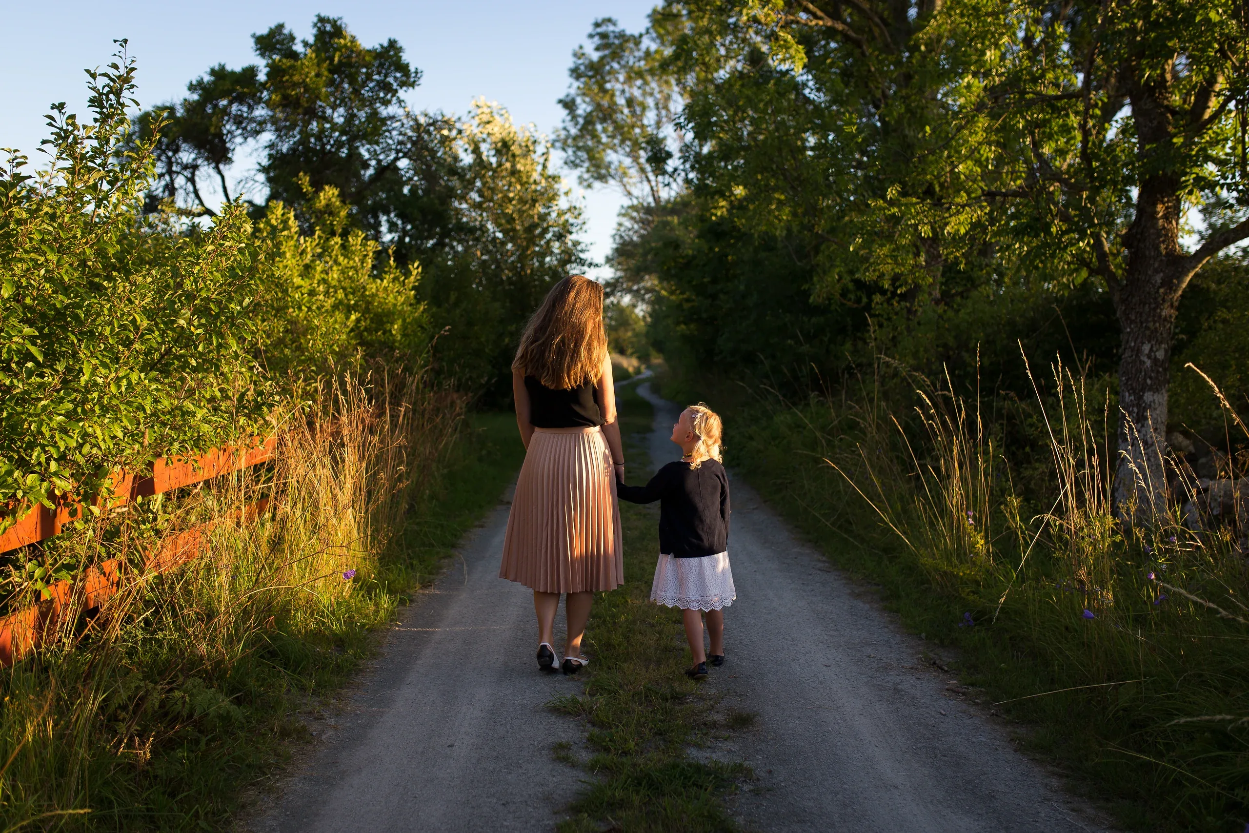 Mother and daughter walking hand in hand down a green country lane