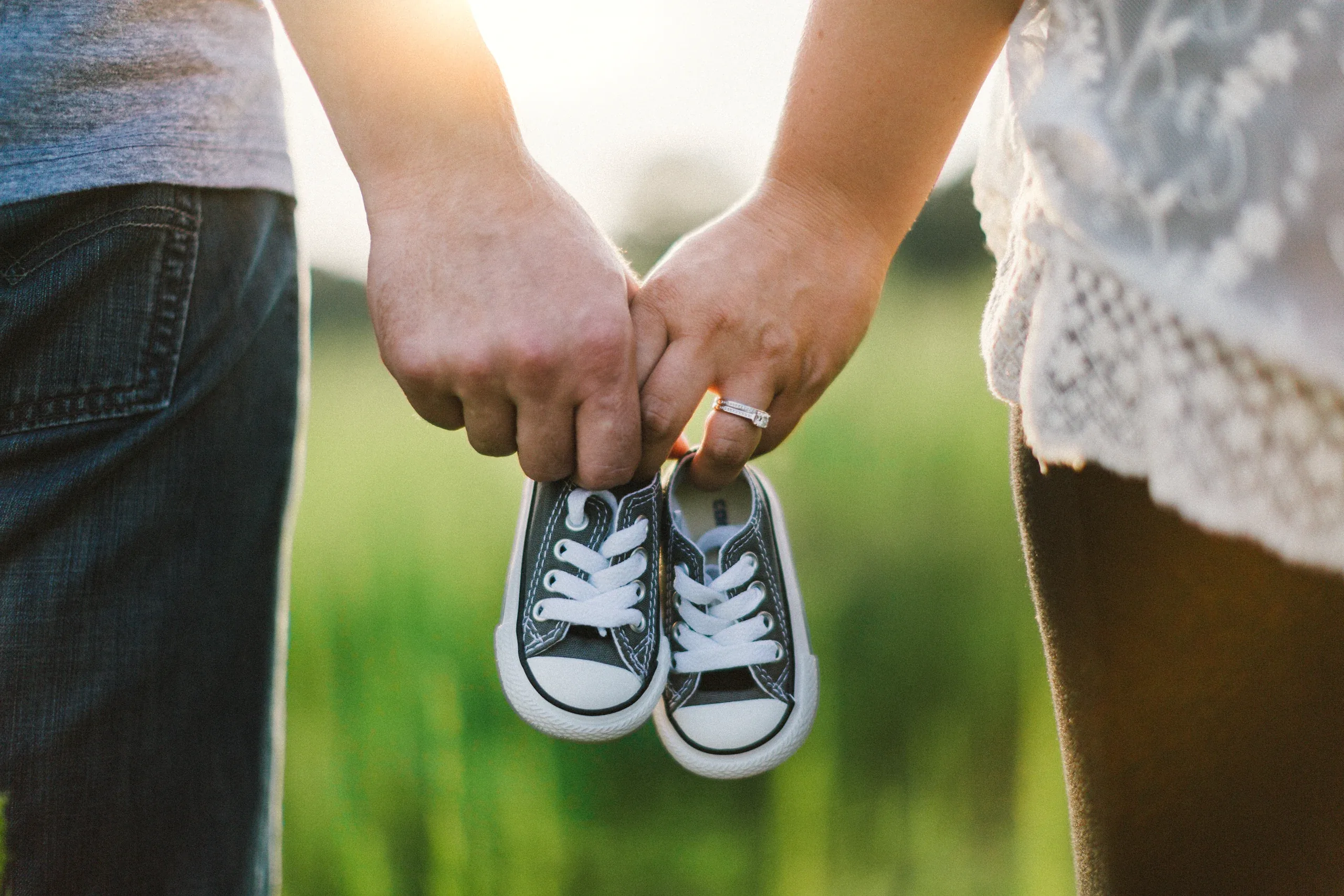 Parents holding a pair of tiny grey trainers between them in the grass