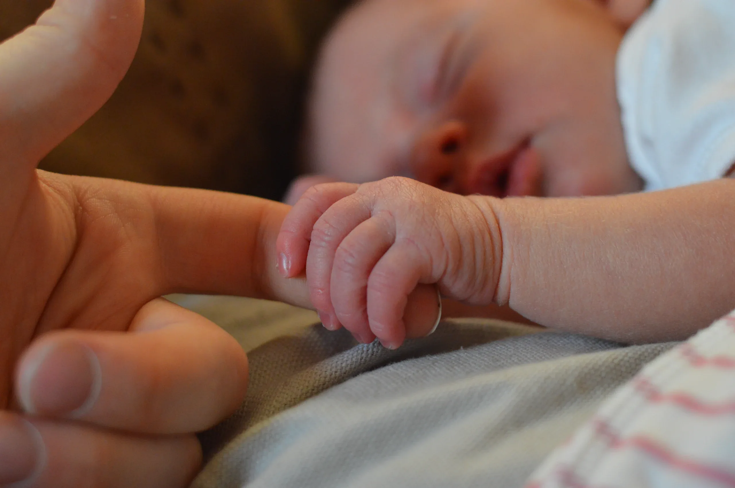 Sleeping newborn gripping a parent’s finger