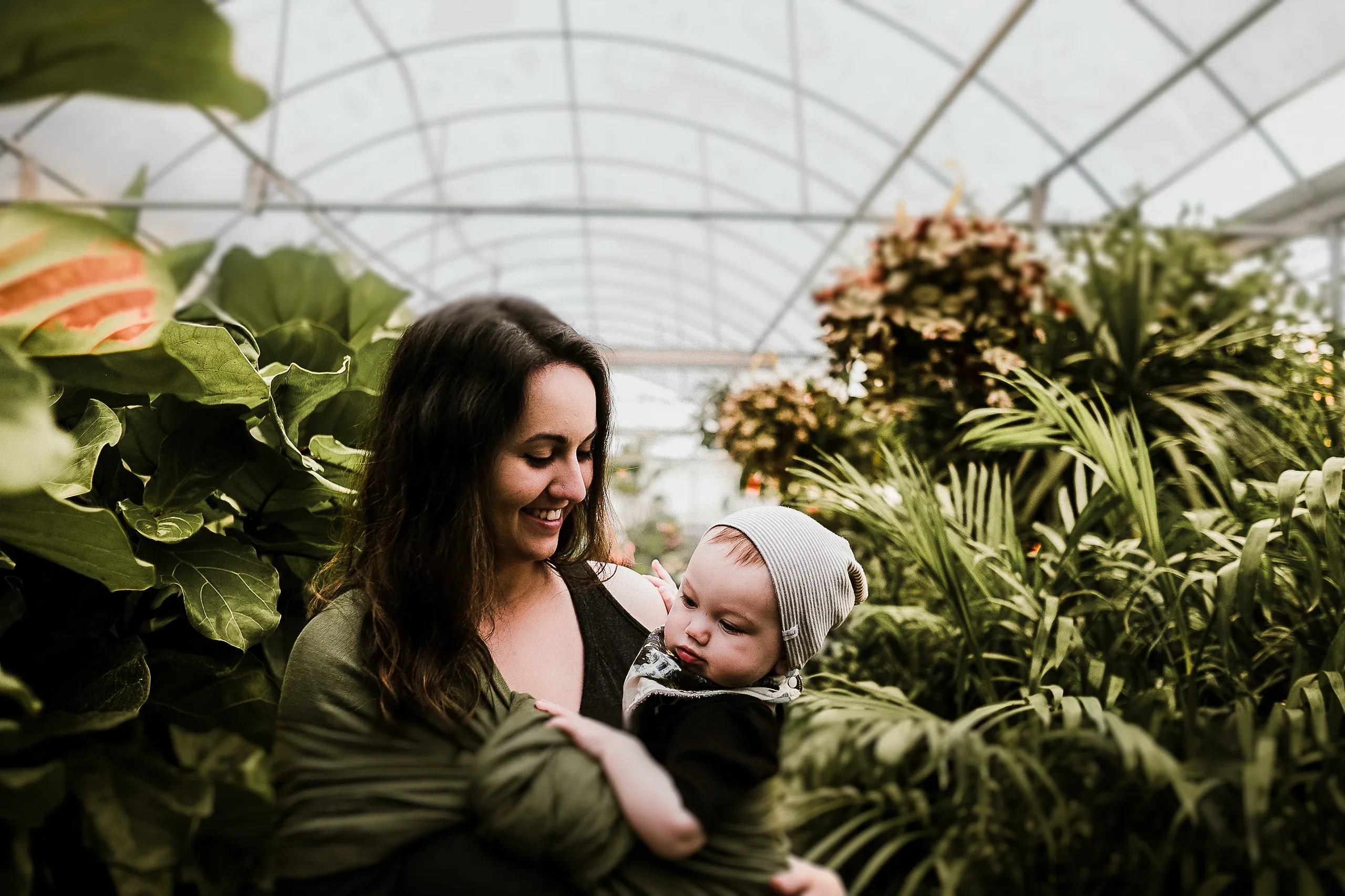 Mother holding her baby in a knitted hat among greenhouse plants