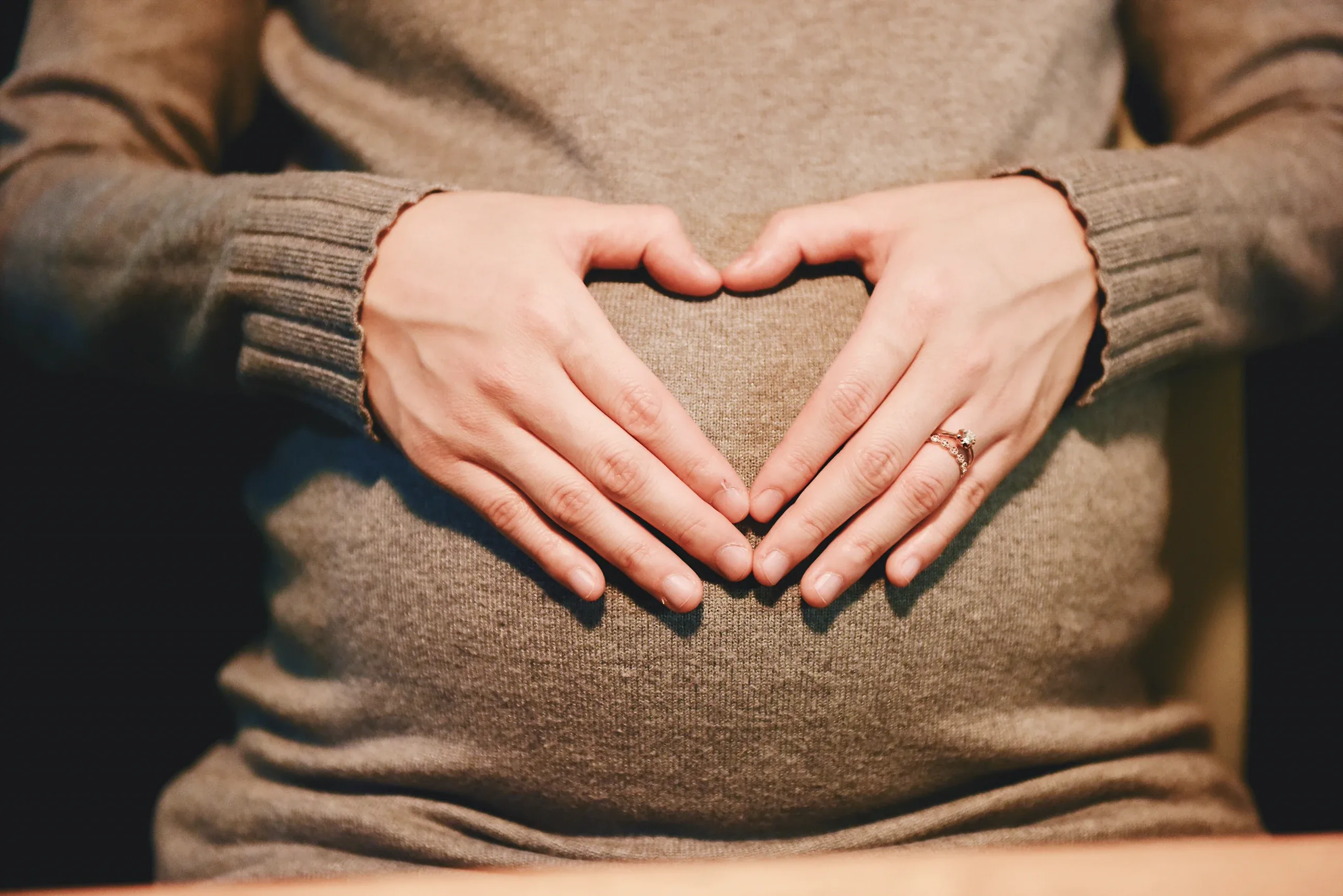 Hands shaping a heart over a bump in a brown knit jumper