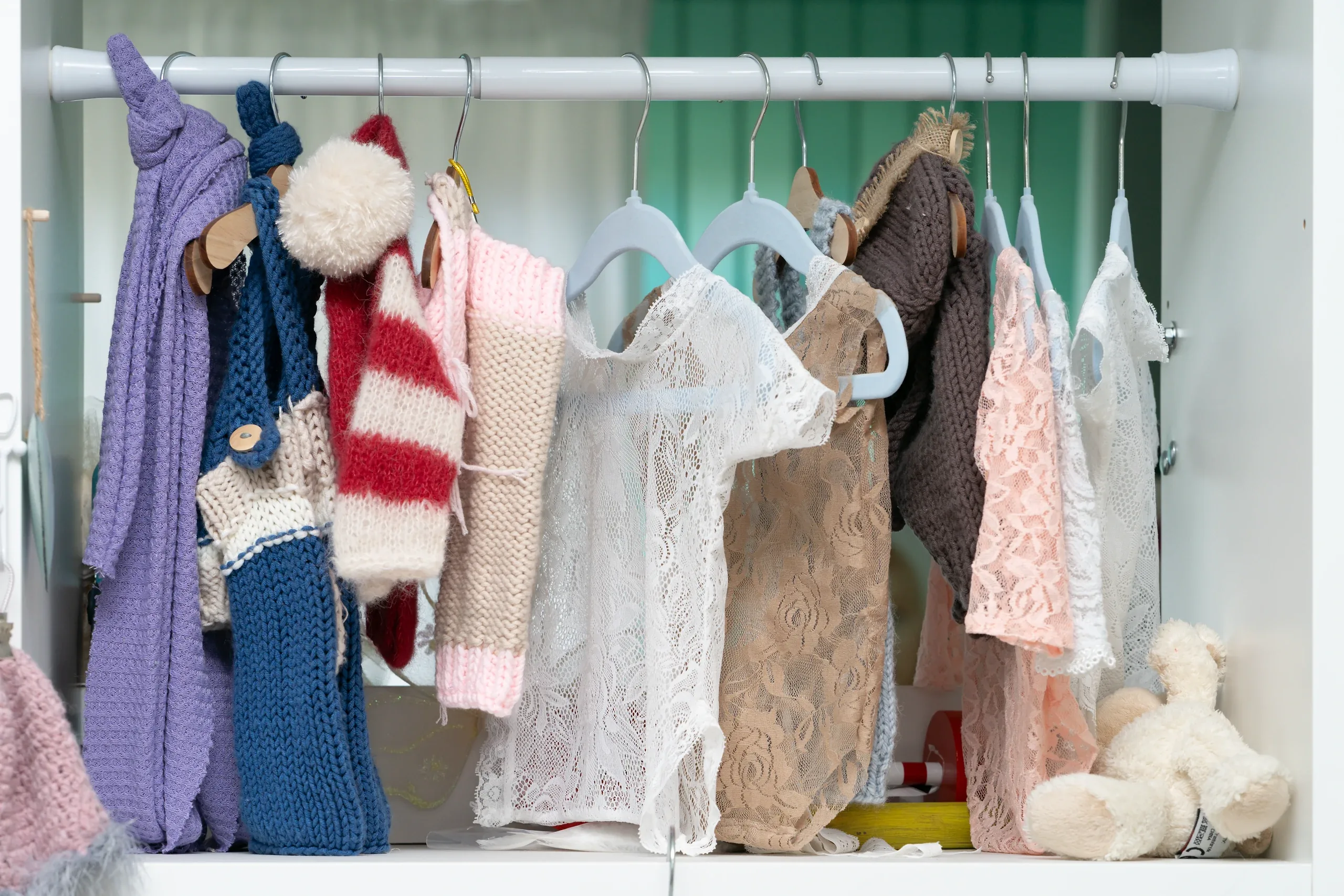 Tiny knitted and lace outfits on hangers in a white nursery wardrobe