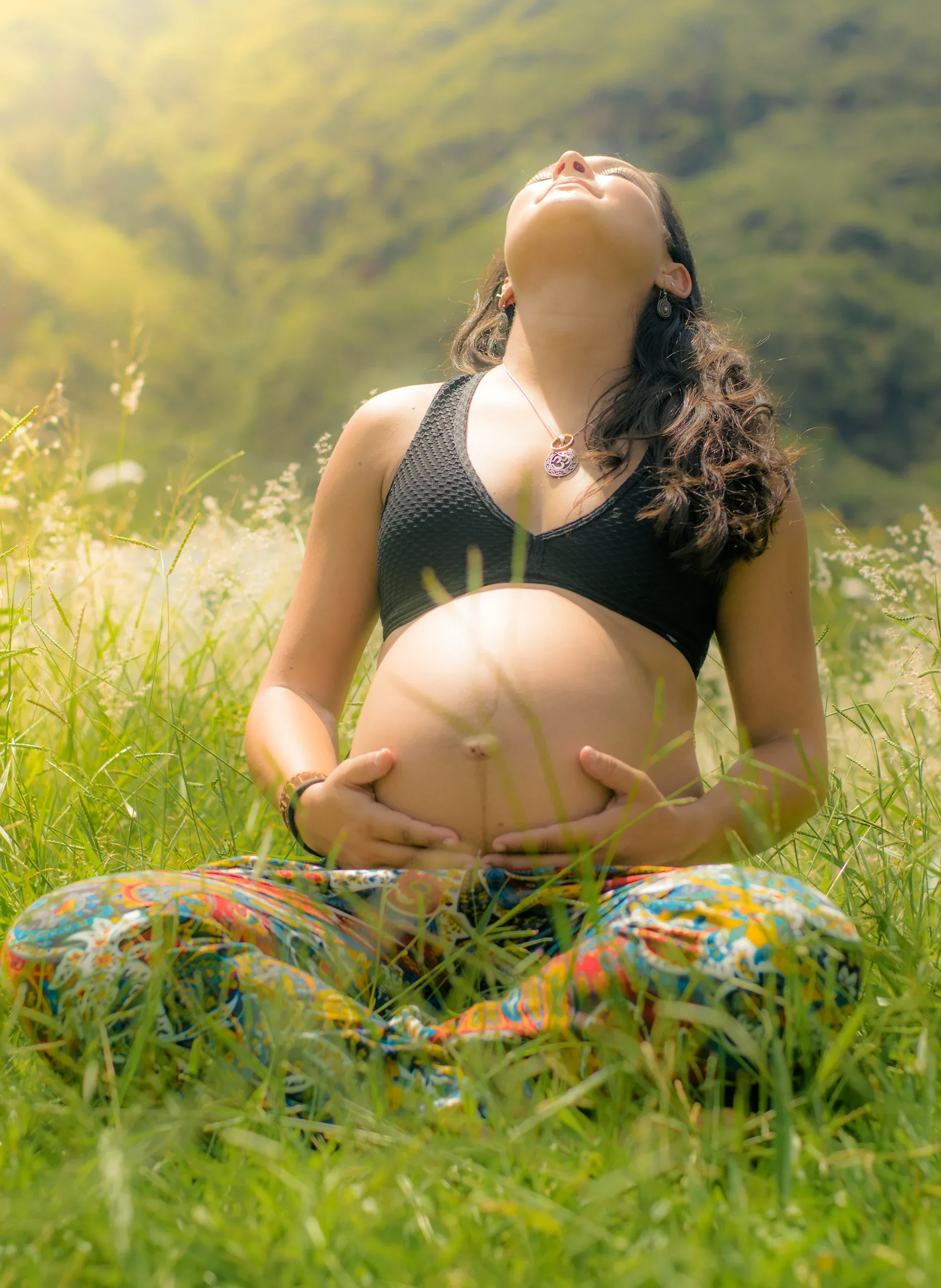 Expecting mother sitting cross-legged in the grass, face turned to the sun