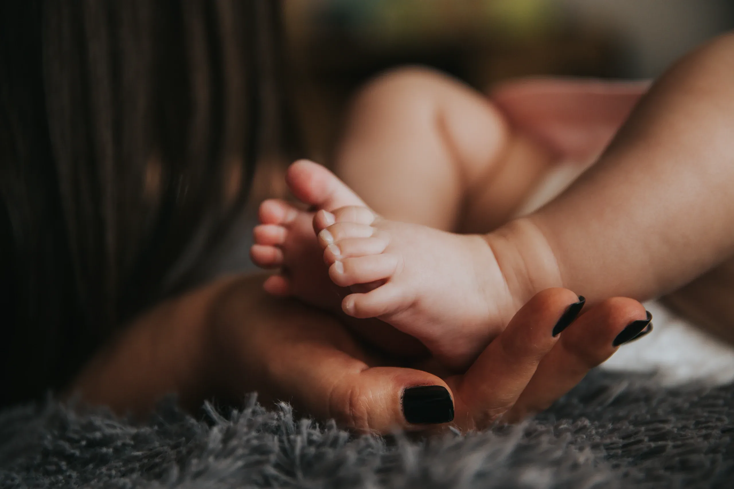 Baby feet in a mother’s hand on a soft grey rug