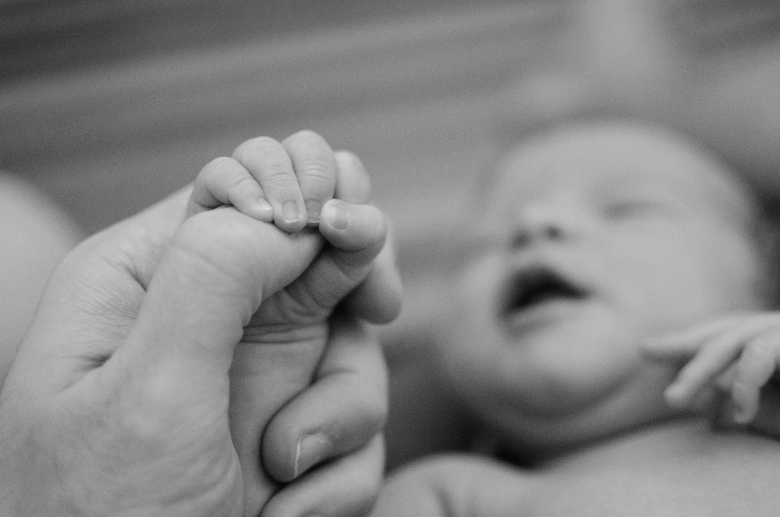Black and white close-up of a newborn gripping a parent’s thumb
