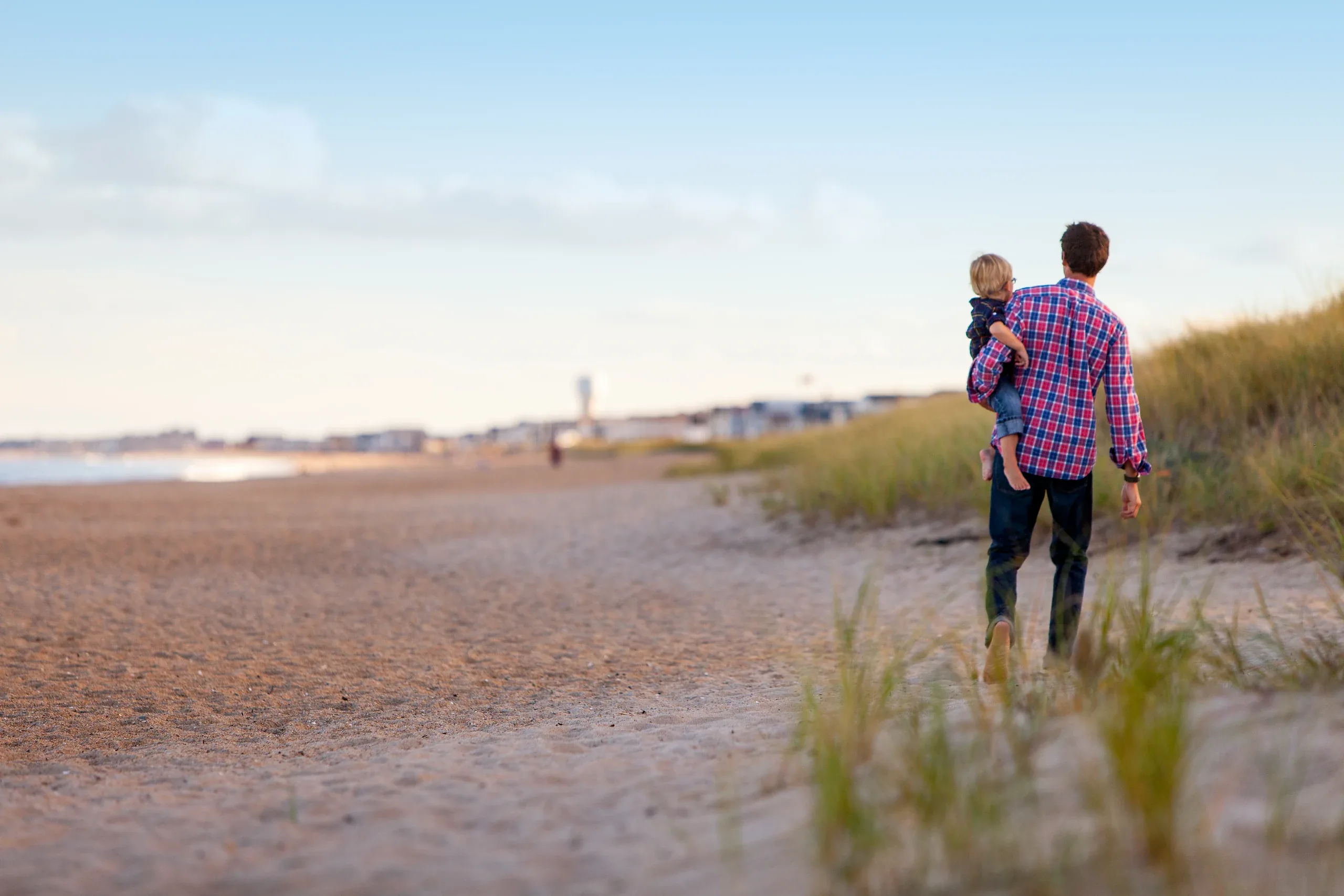 Father carrying his toddler along a dune path by the sea