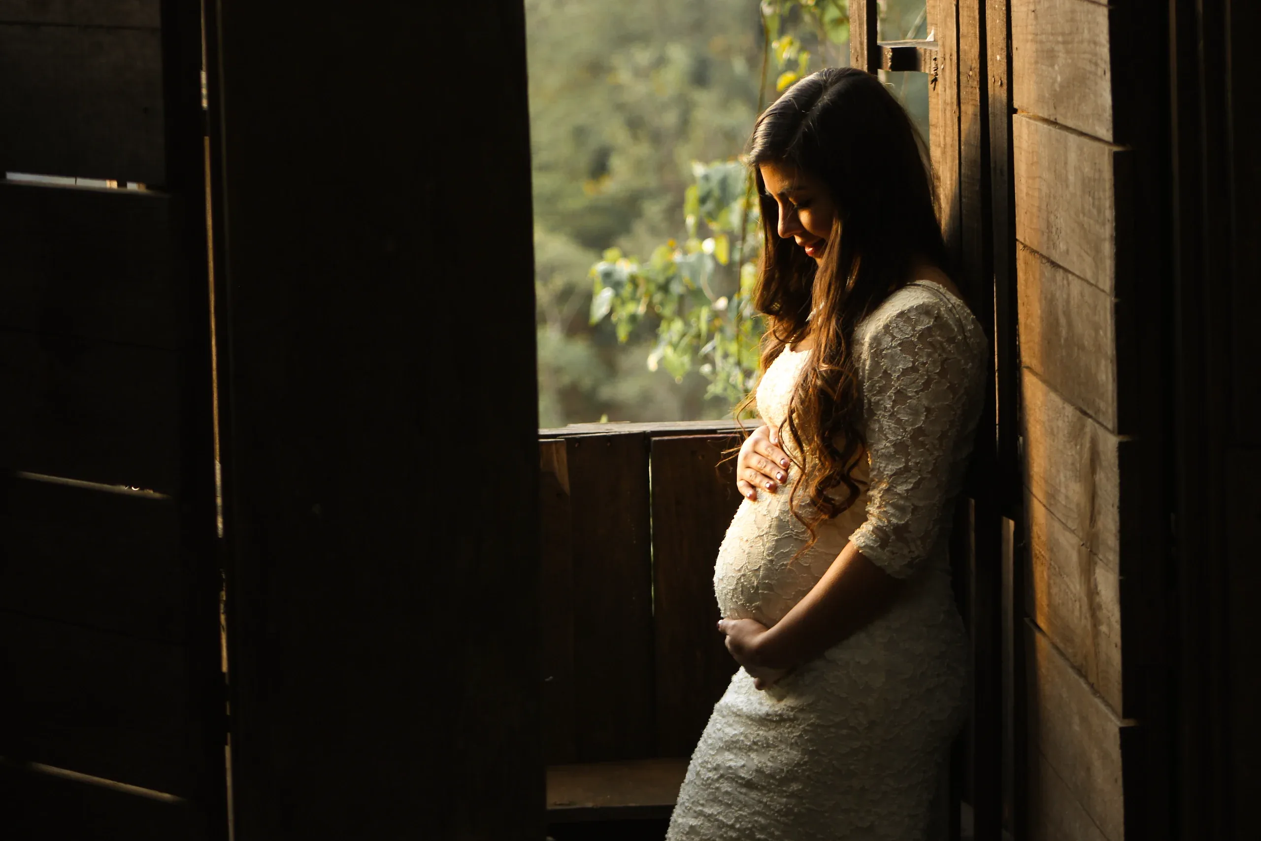 Pregnant woman leaning in a wooden doorway, hands on her bump