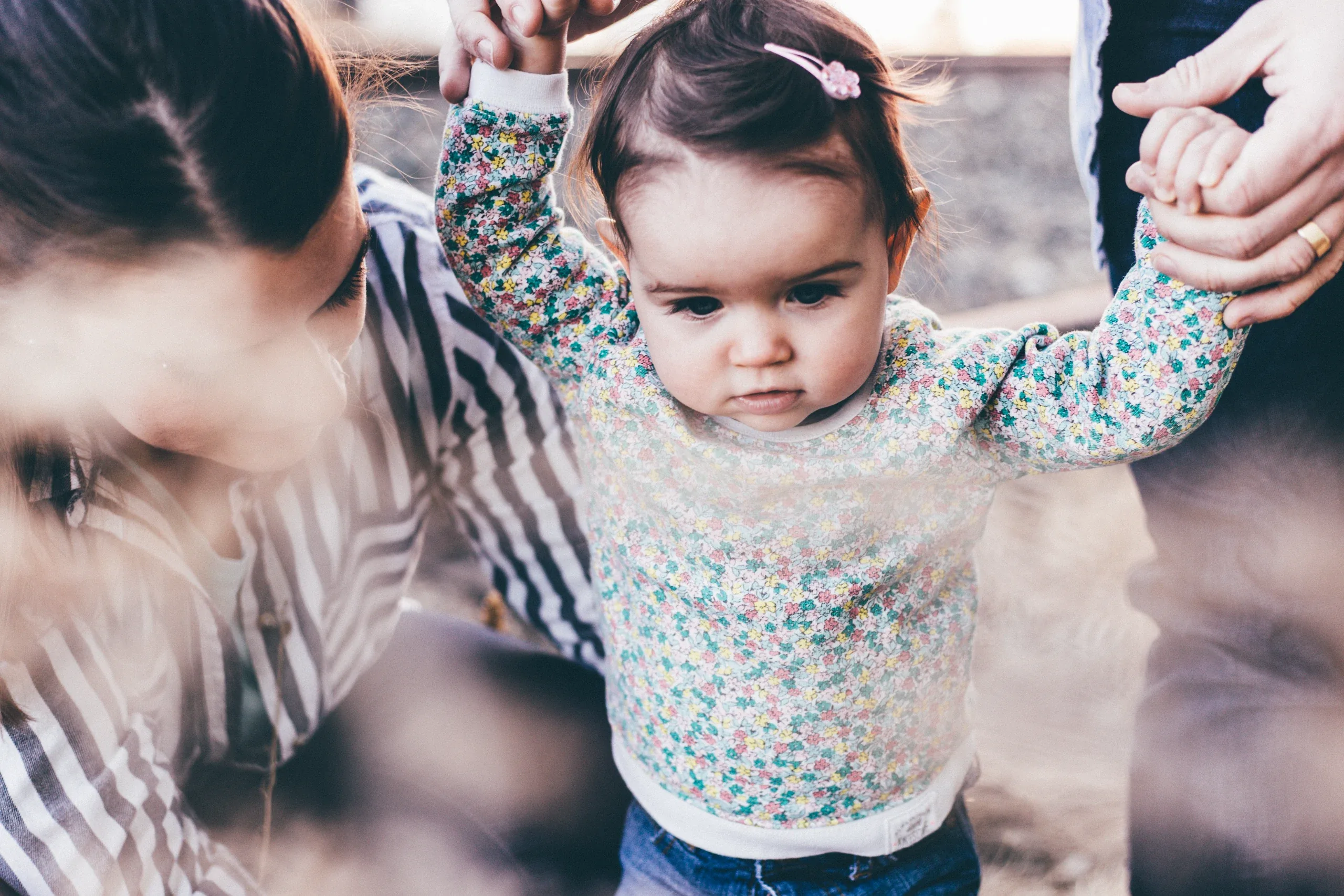 Toddler taking steps while her parents hold both her hands