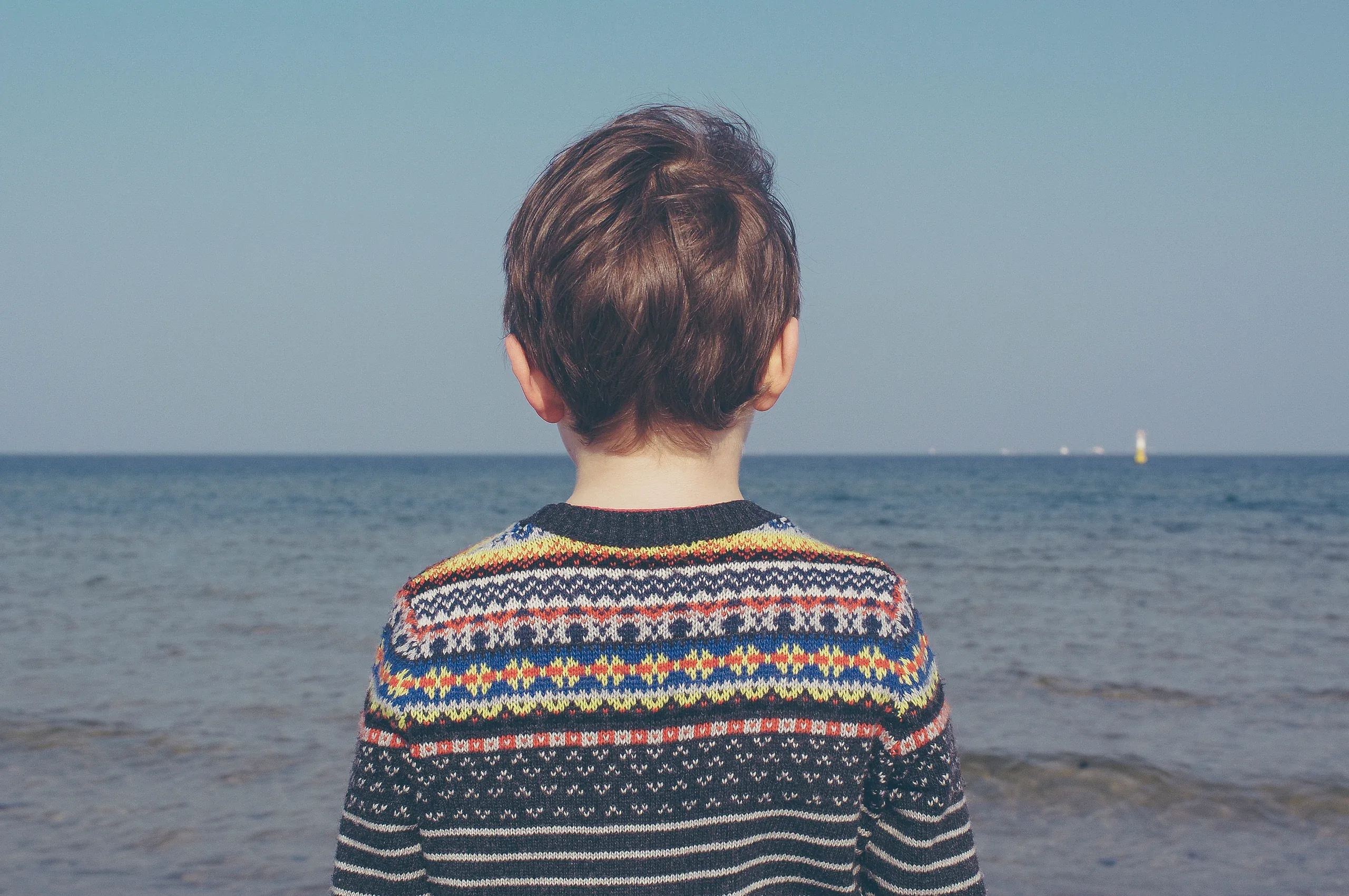 Boy in a patterned jumper looking out to sea