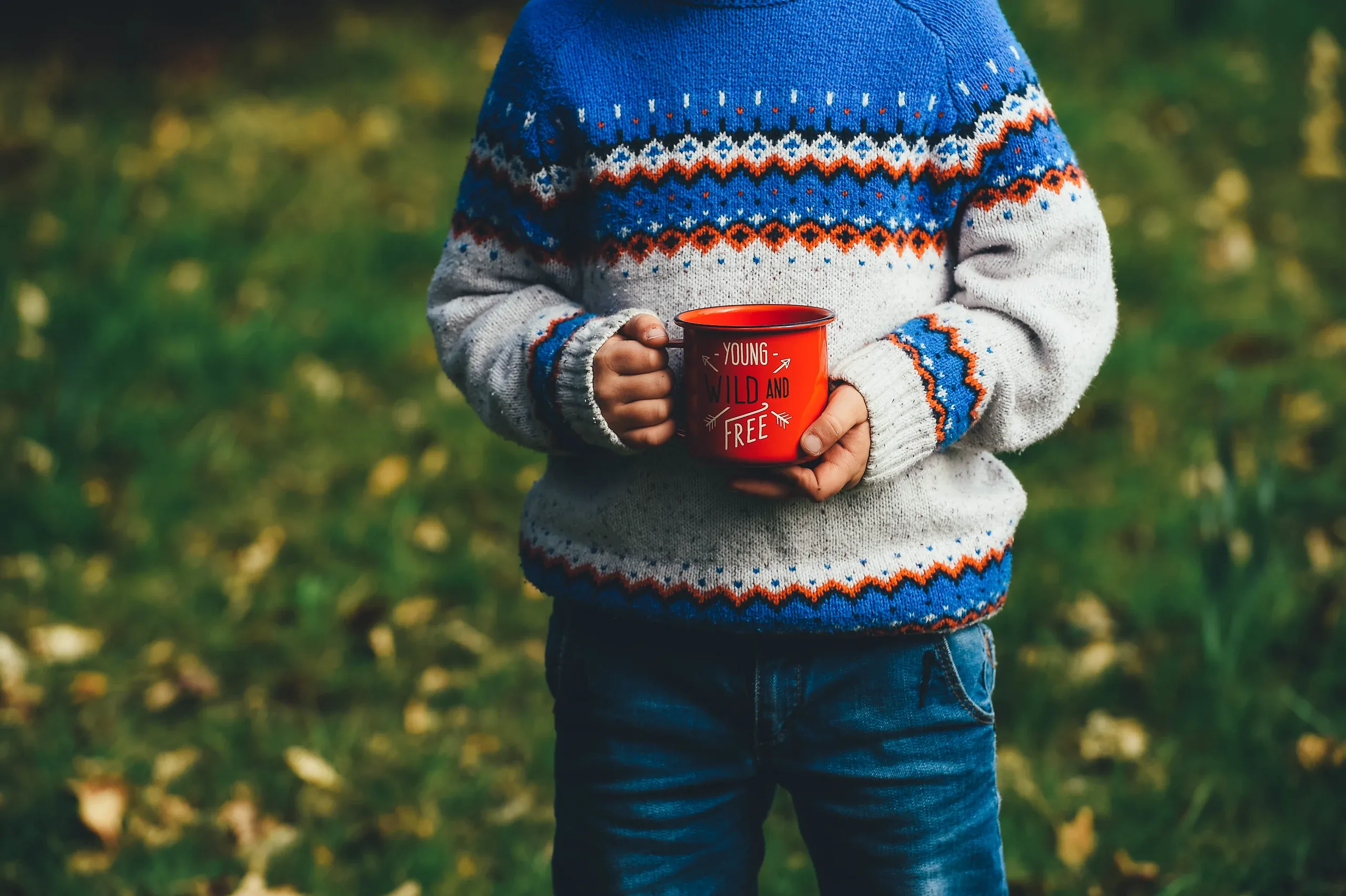 Child in a Fair Isle jumper holding a red enamel mug