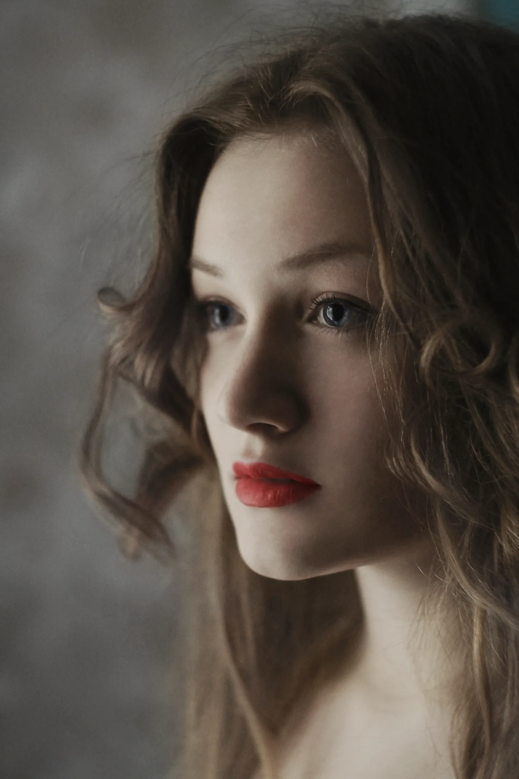 Woman with soft curls and red lipstick in profile against a mottled grey backdrop
