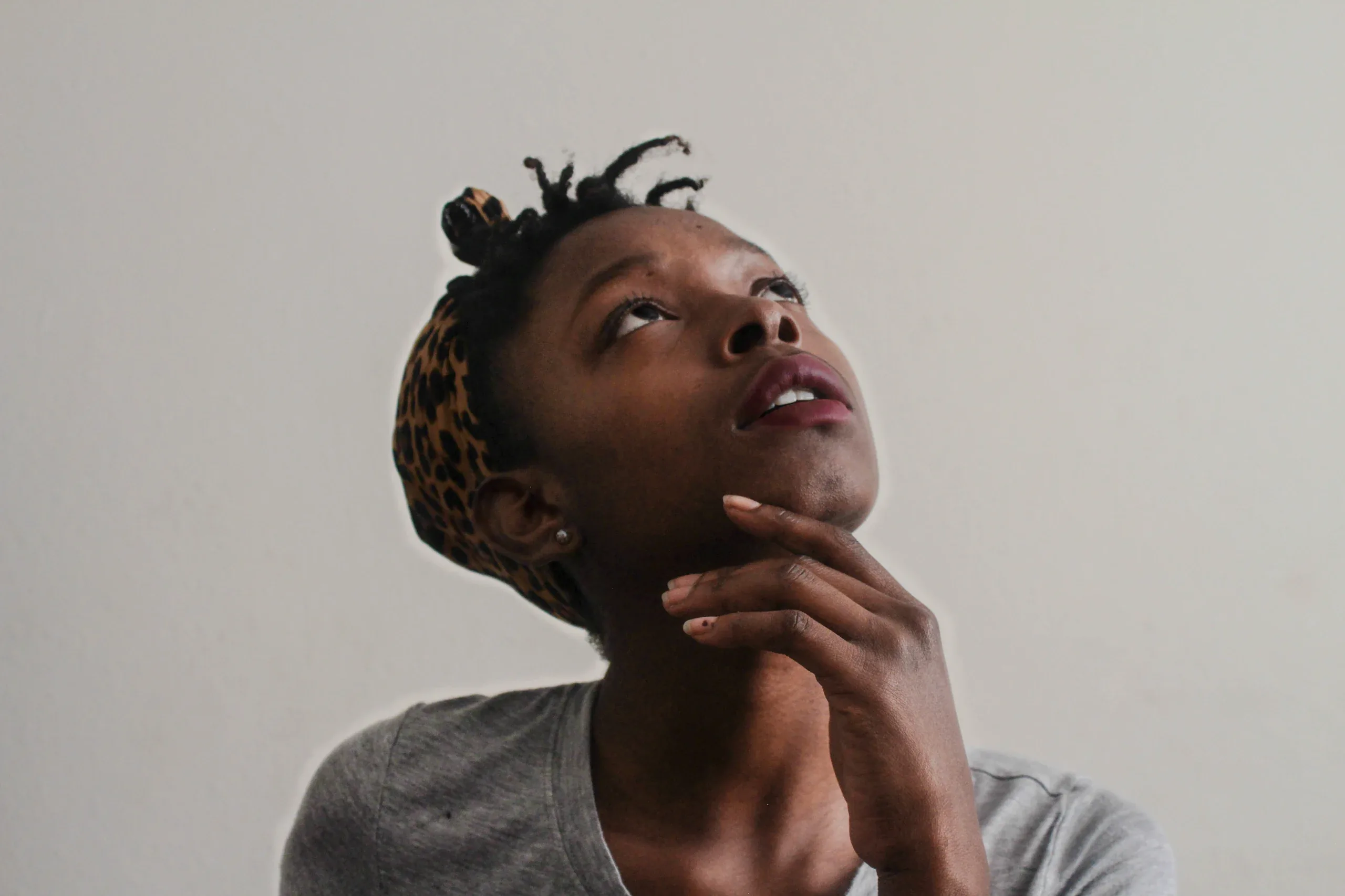 Woman with a leopard print headband resting her chin on her hand, looking up, on a plain wall