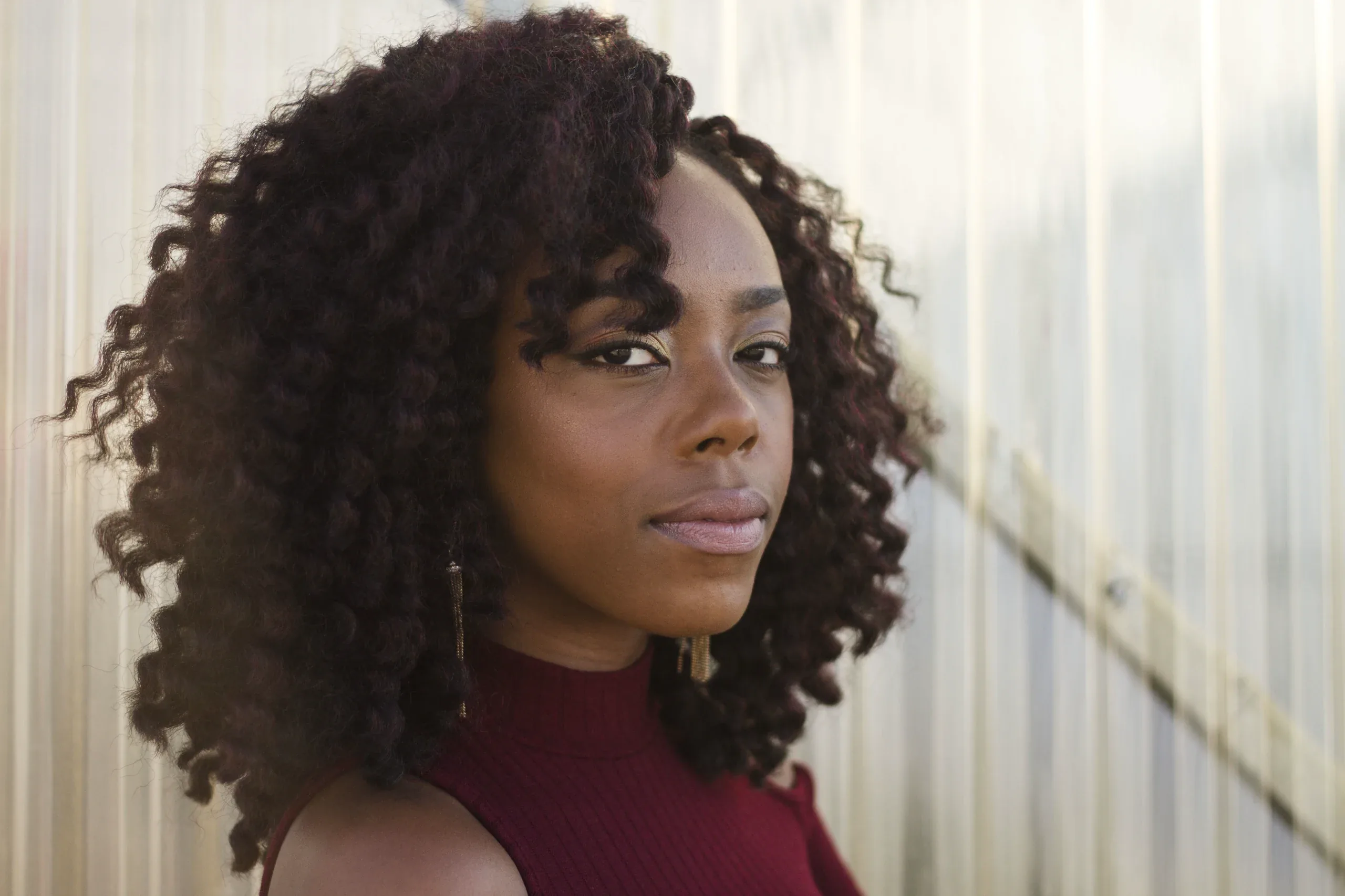Woman with long dark curls in a burgundy top looking straight at the camera