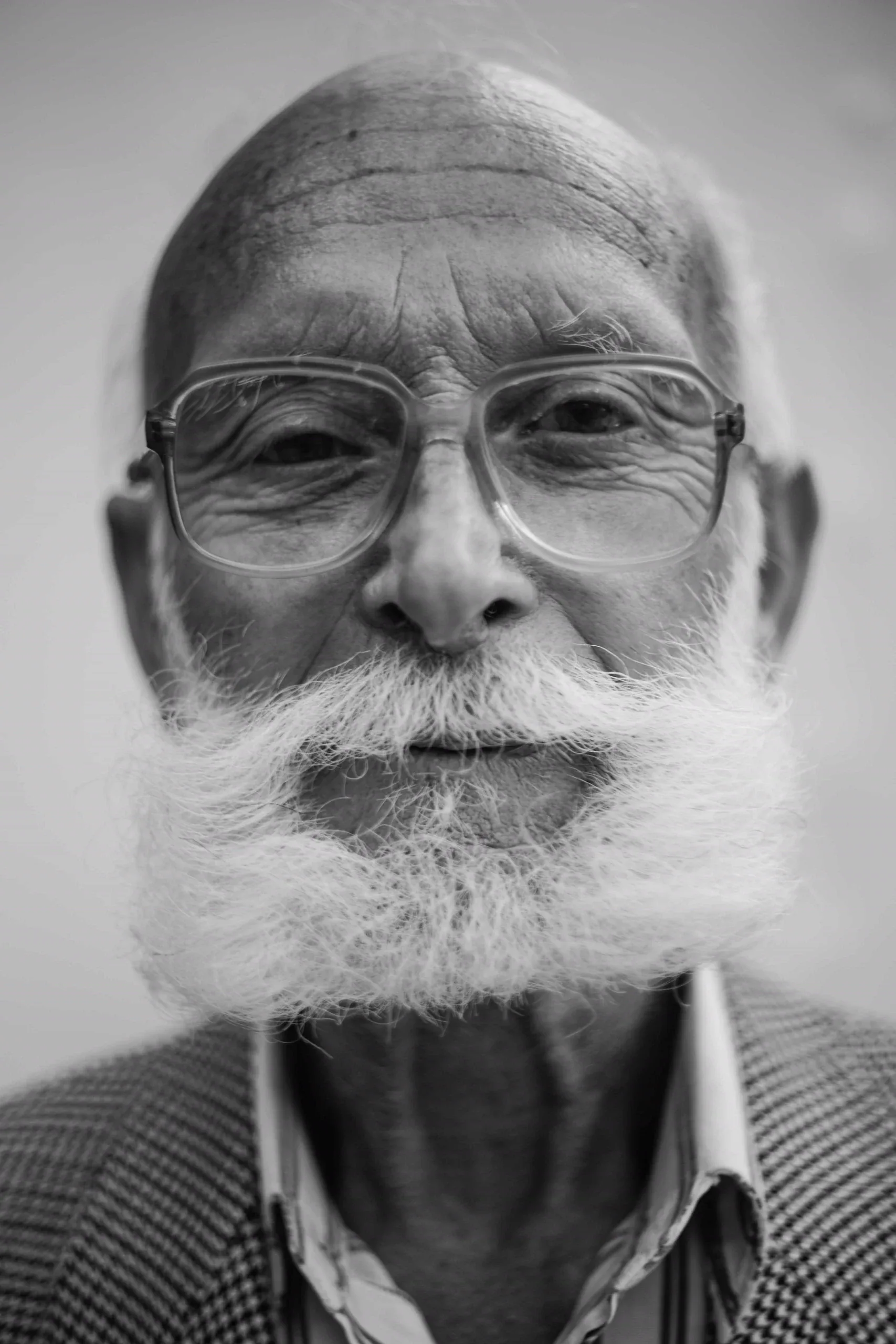 Black and white close portrait of an older man with a white moustache and large glasses