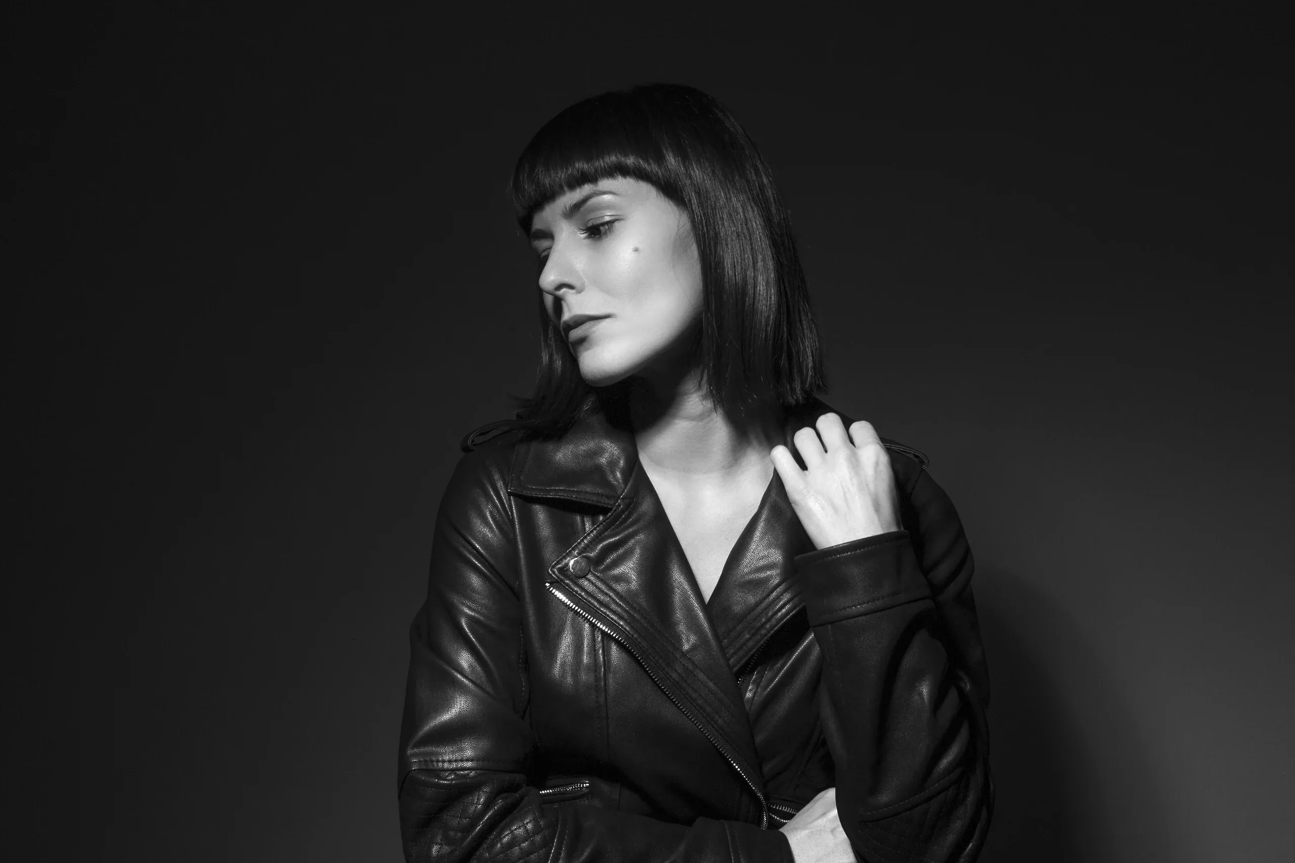 Black and white studio portrait of a woman with a fringe in a leather jacket, eyes lowered