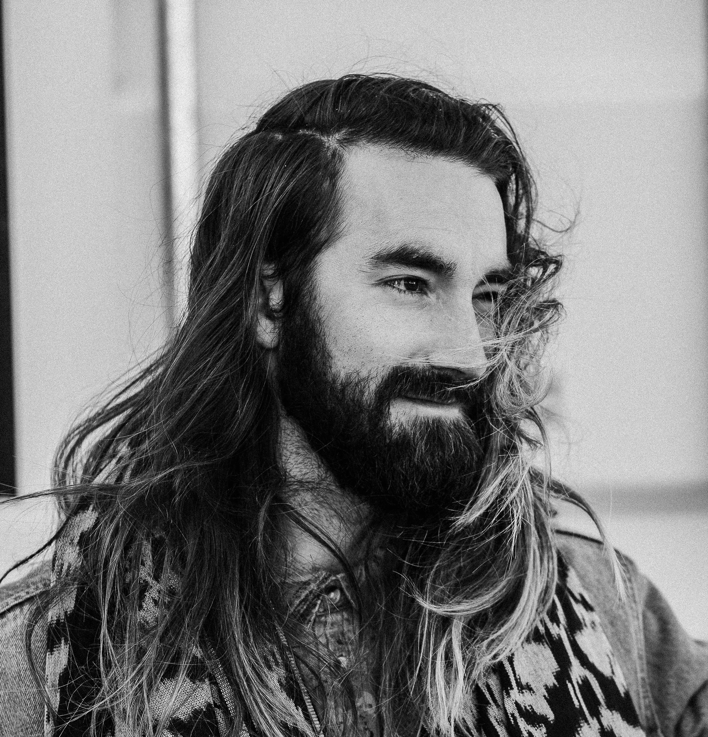 Black and white portrait of a man with long hair and a full beard, glancing sideways