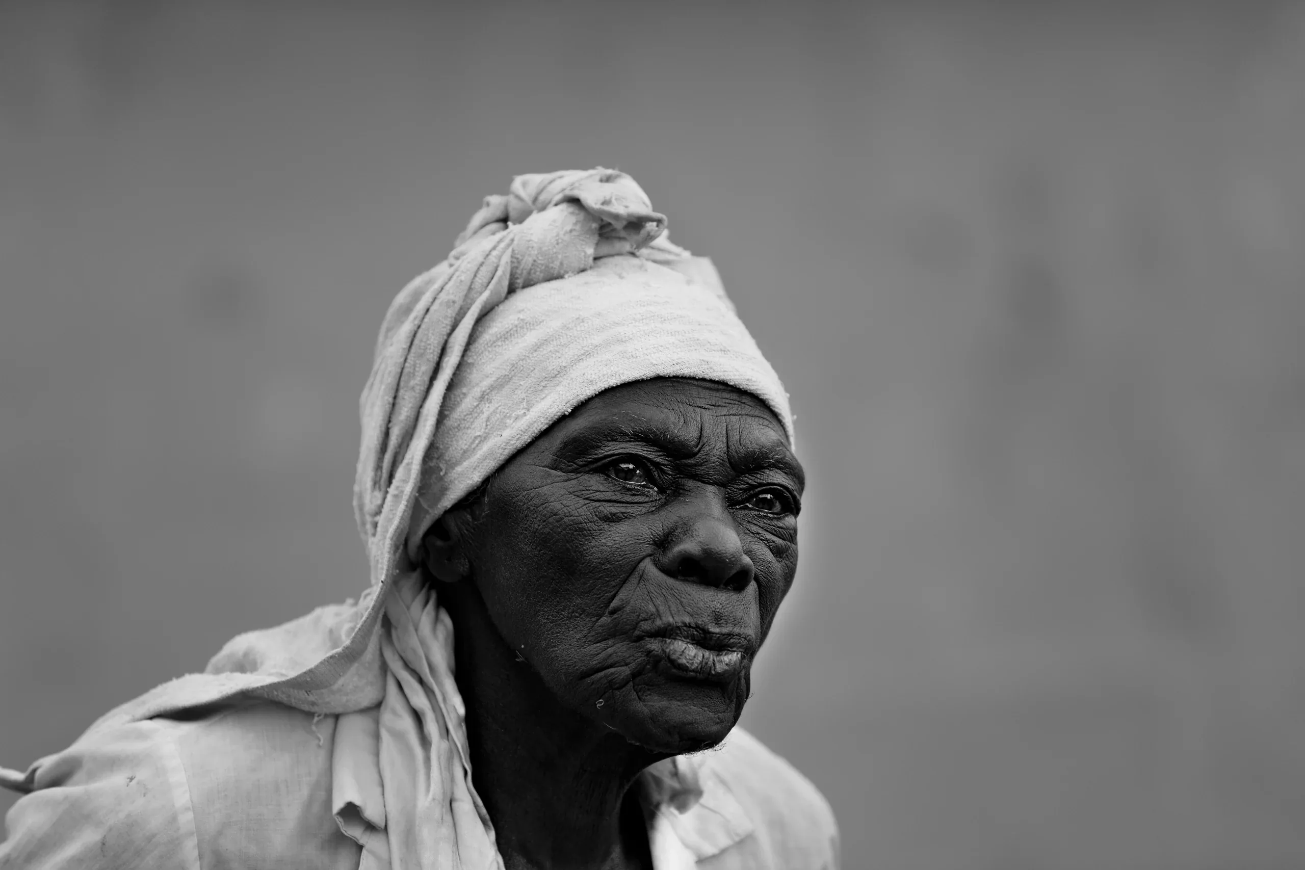 Black and white portrait of an elderly woman in a headscarf against a grey wall