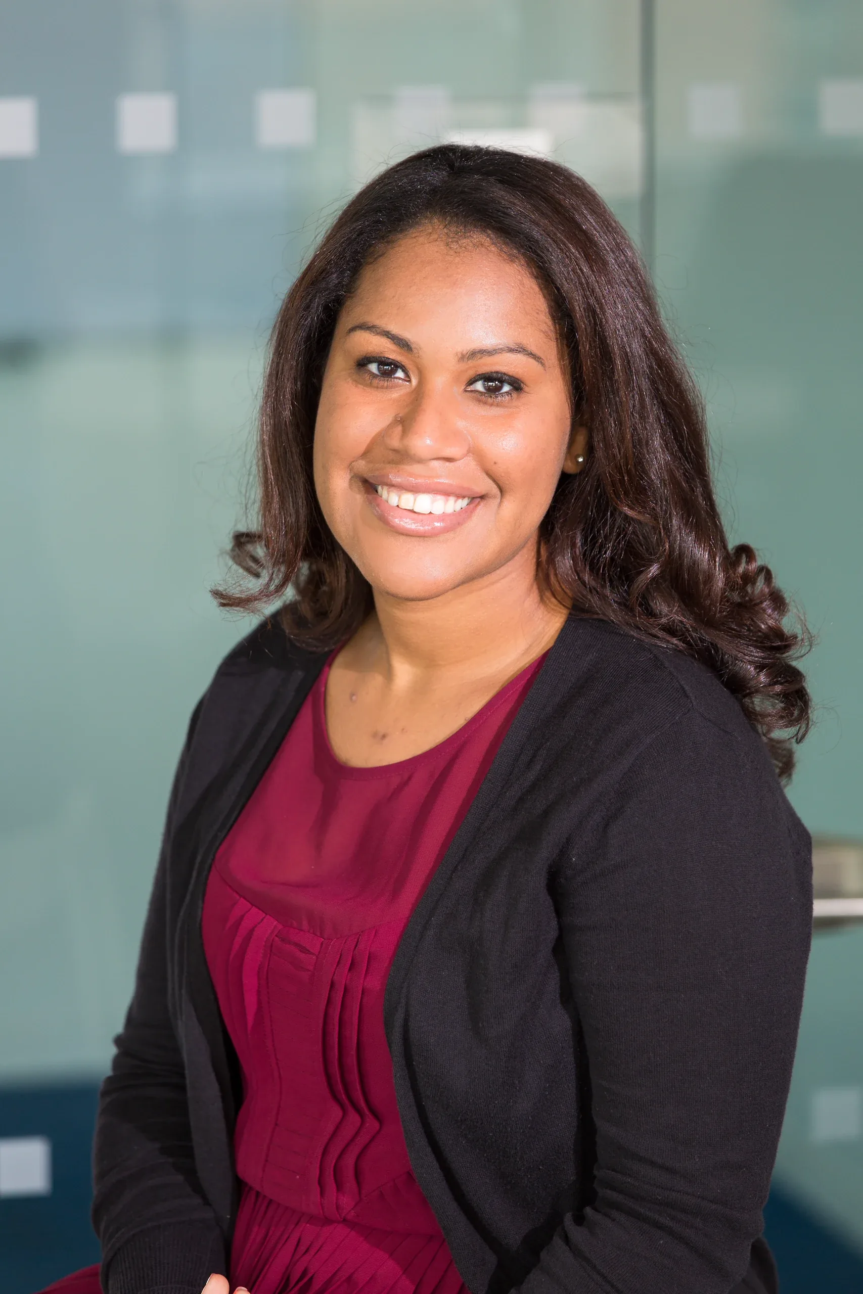 Smiling woman in a black cardigan and burgundy top in a glass-walled office