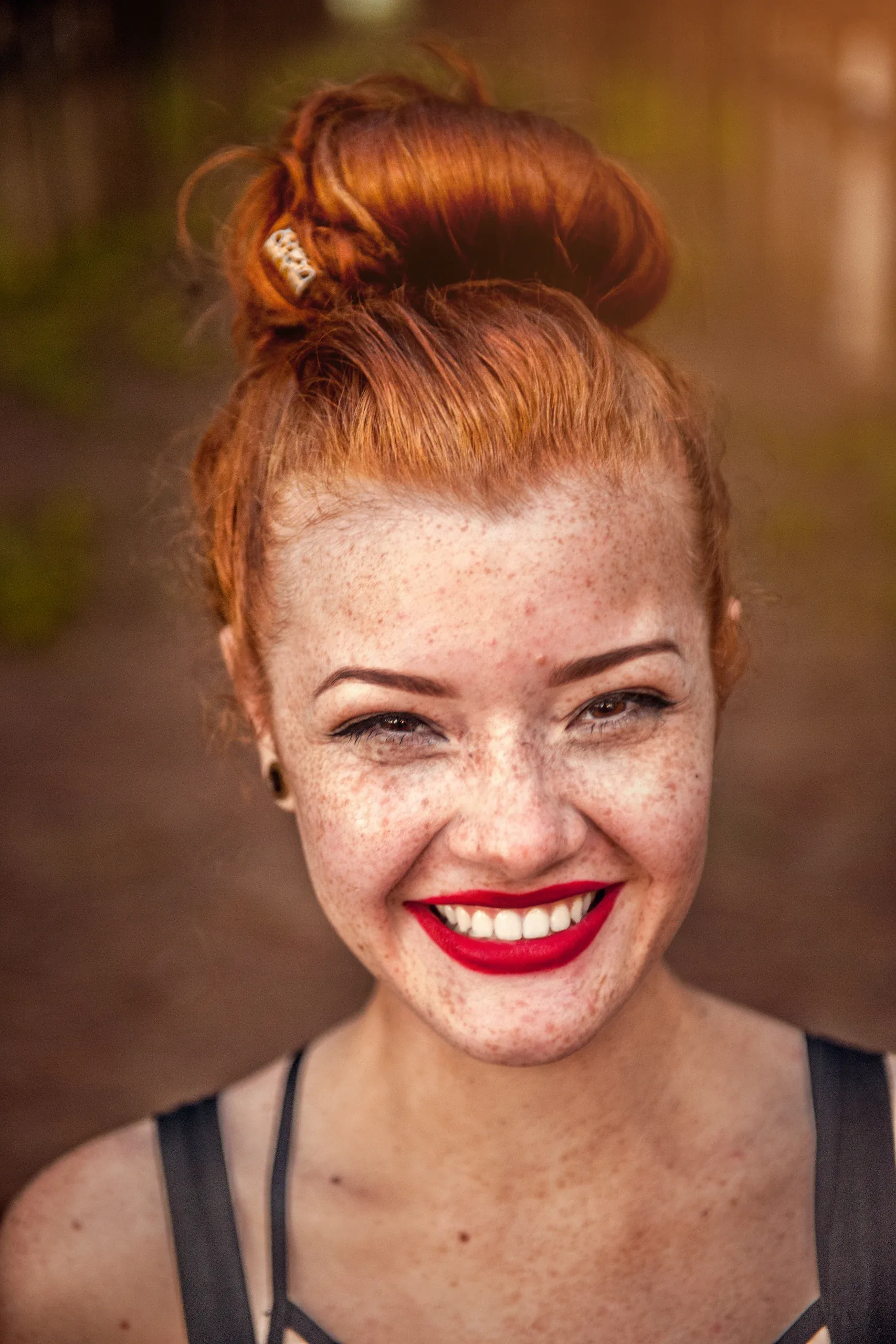 Red-haired woman with freckles and red lipstick smiling broadly, hair in a top knot