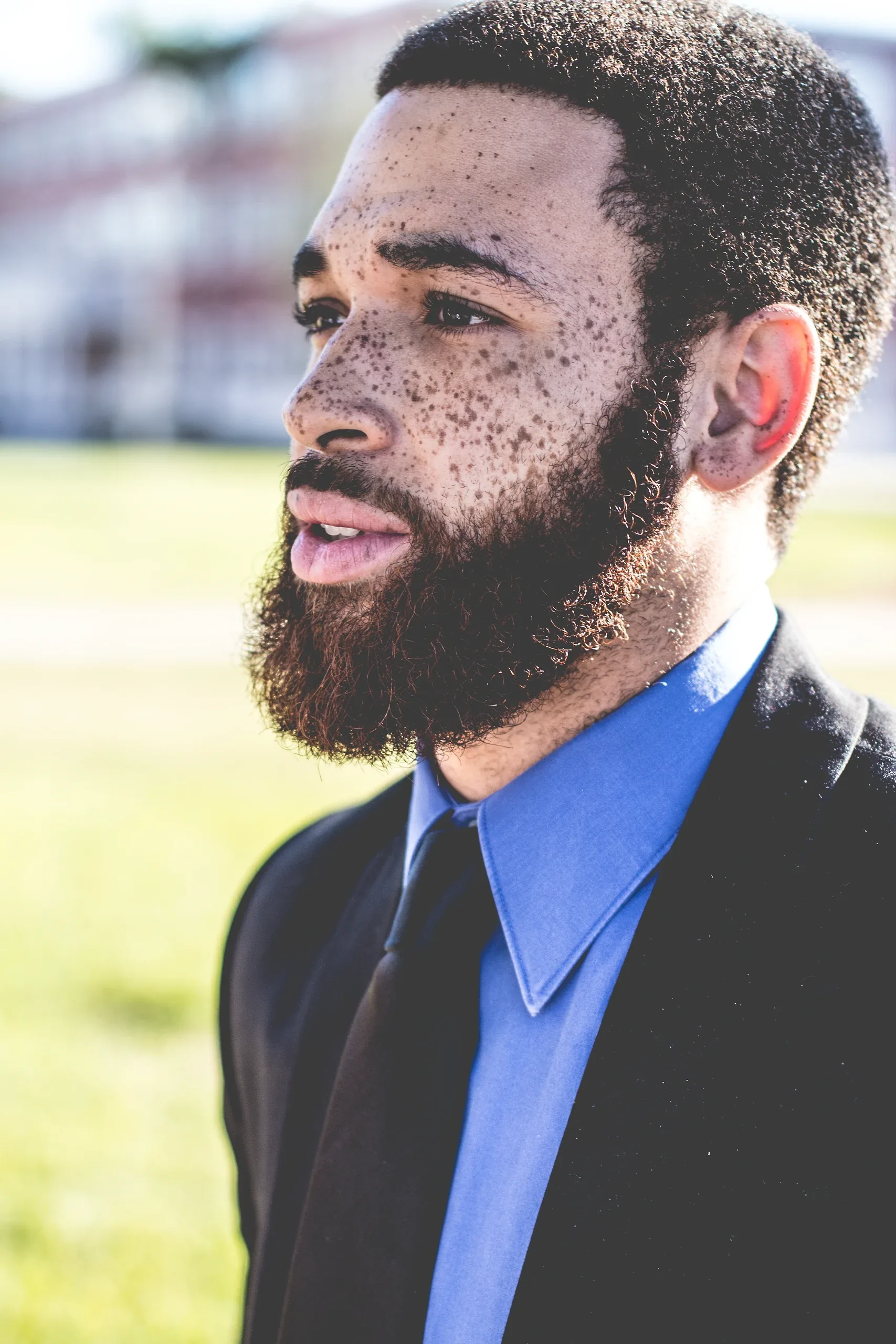 Bearded man in a dark suit and blue shirt looking off to the side outdoors