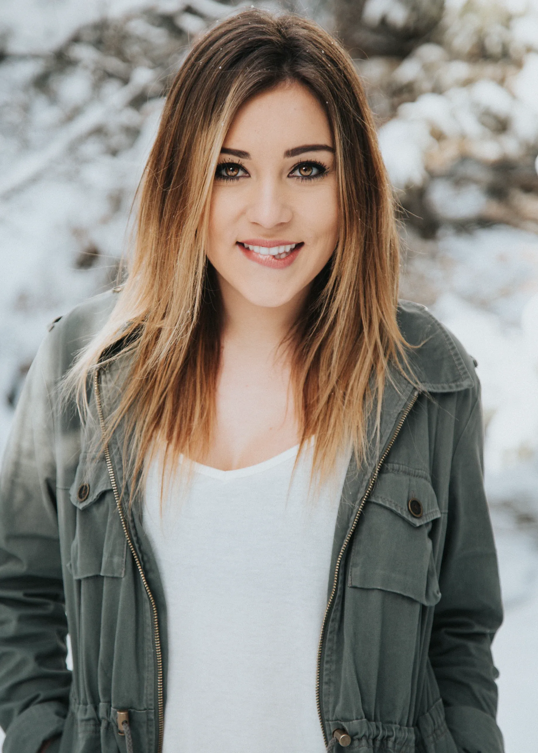 Smiling woman with long highlighted hair in an olive field jacket, outdoors in winter