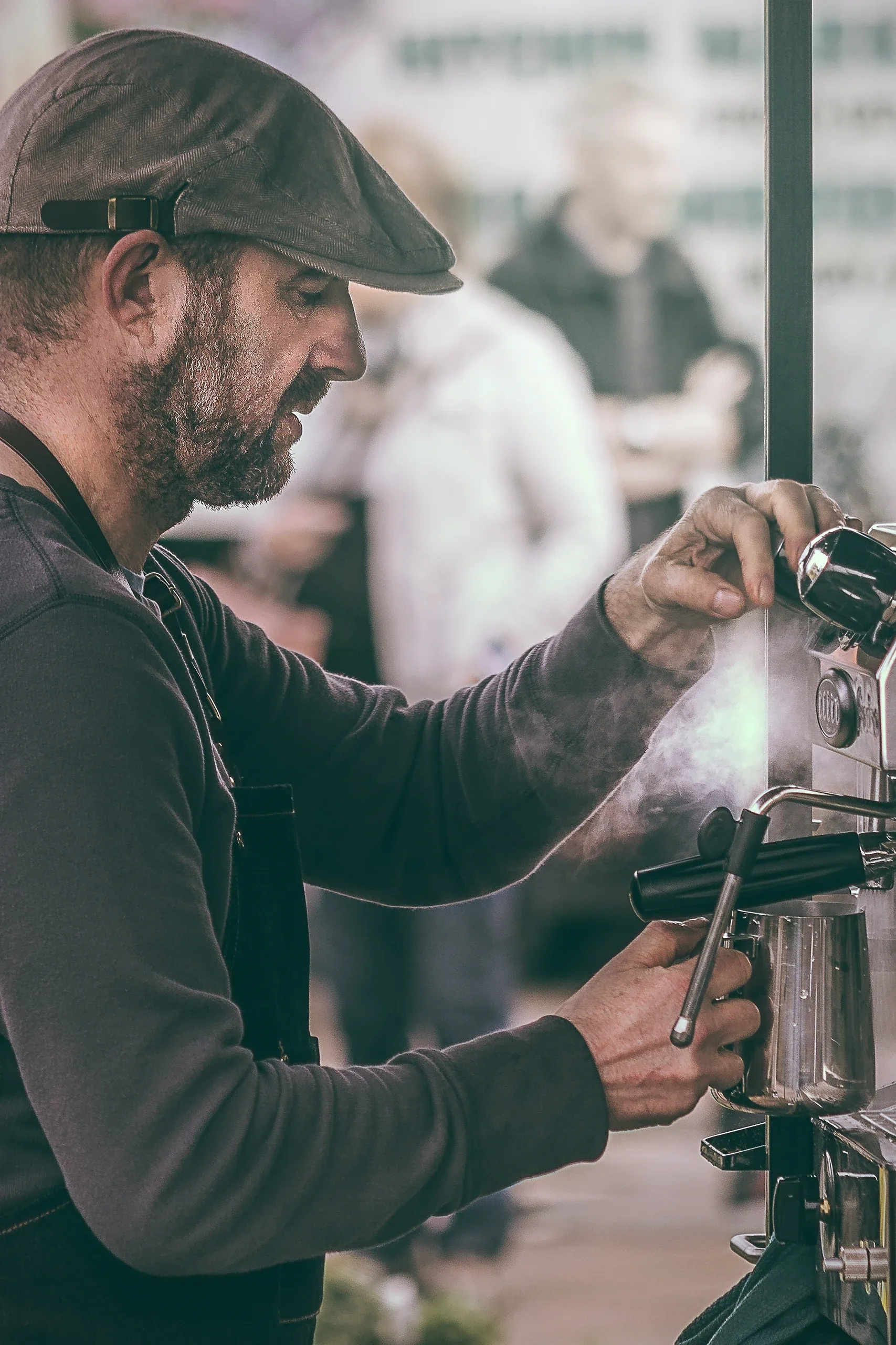 Barista in a flat cap steaming milk at an espresso machine
