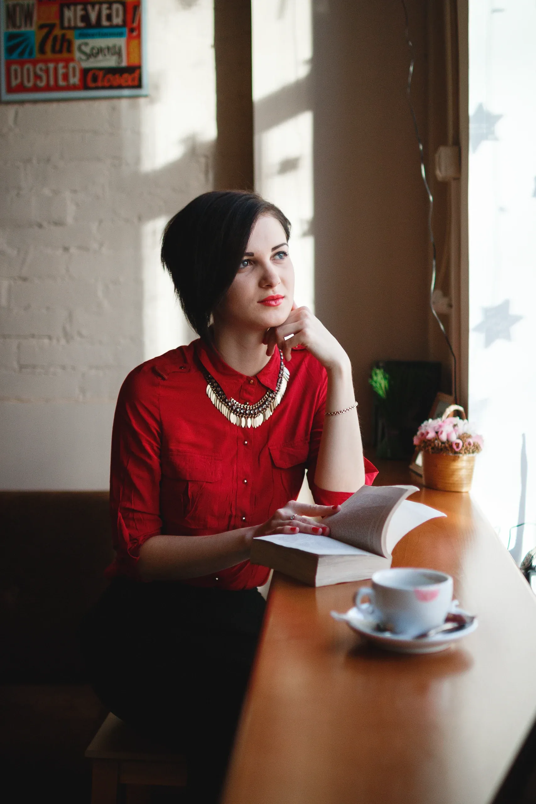 Woman in a red shirt with a book and a cup of tea at a café window